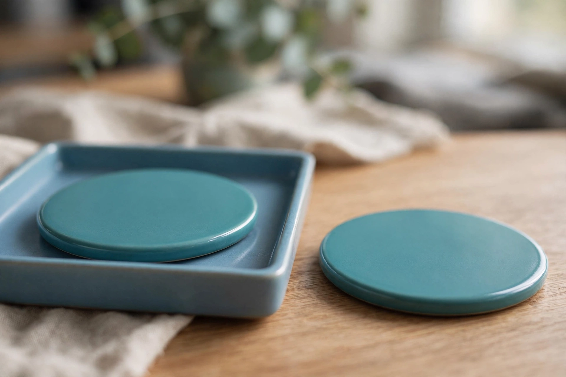 Two identical teal ceramic discs are shown on a wooden desk; one disc is inside a blue tray, and the other is placed separately next to it.