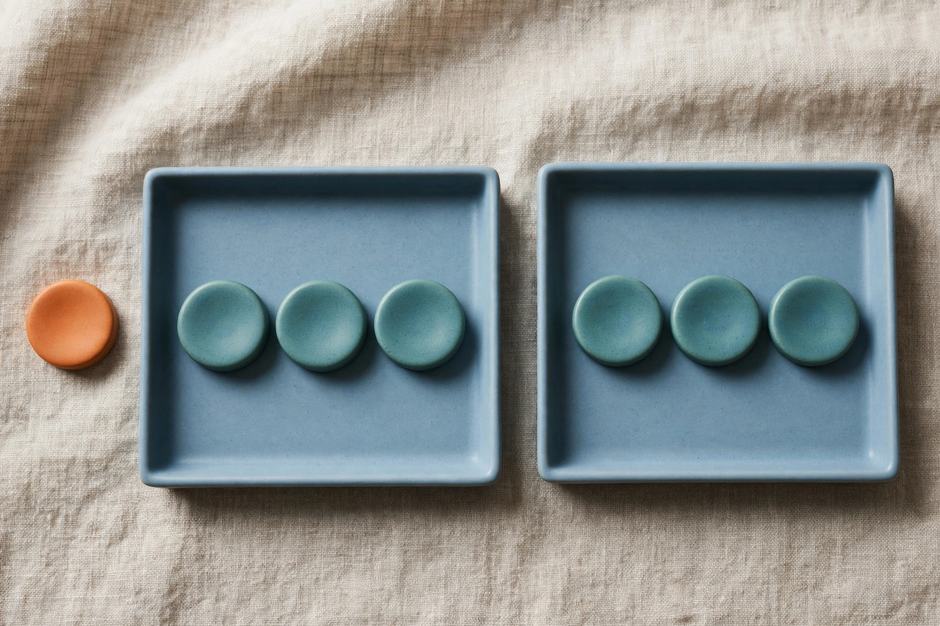 Two blue trays each hold three teal tokens, with a single orange token placed beside the left tray.