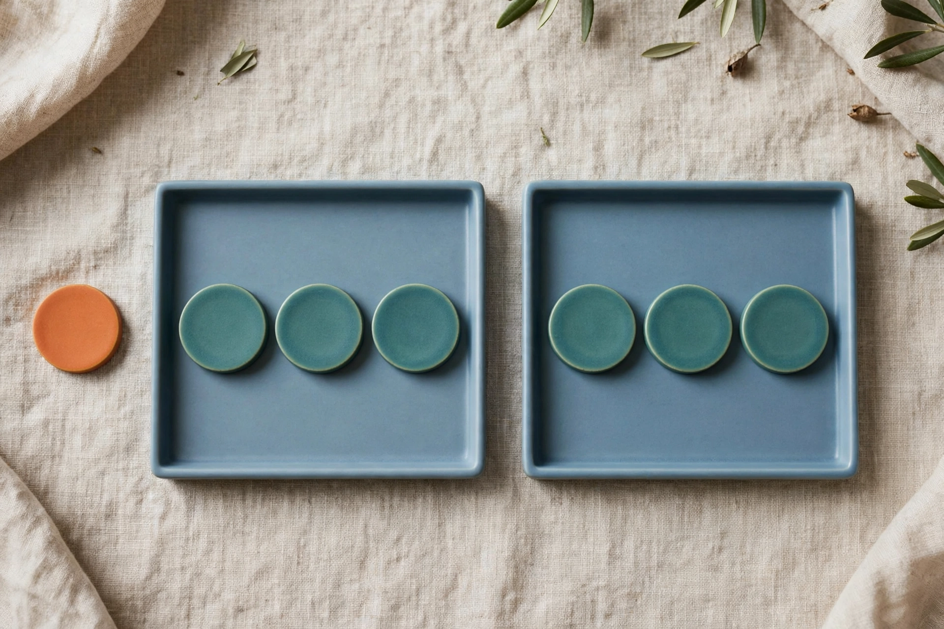 Two blue trays each hold three teal ceramic tokens, with a single orange token placed beside the left tray.