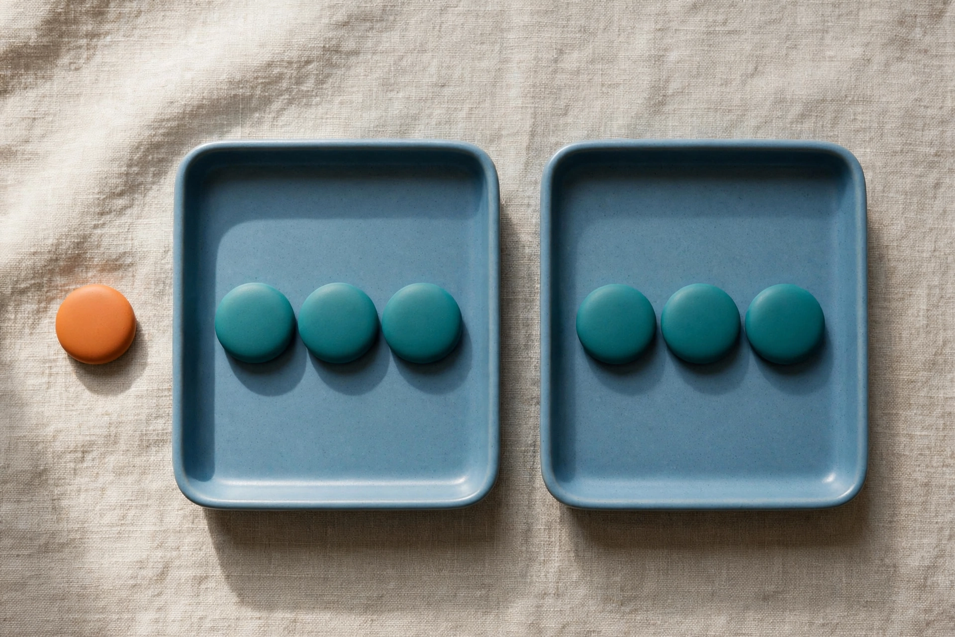 Two blue trays hold teal tokens, with an orange token beside one tray on a textured surface.