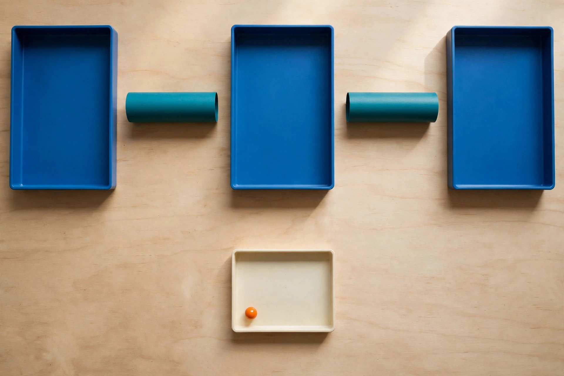 Three blue trays and two teal cylinders are arranged on a wooden surface, with a fourth ivory tray containing an orange bead below.