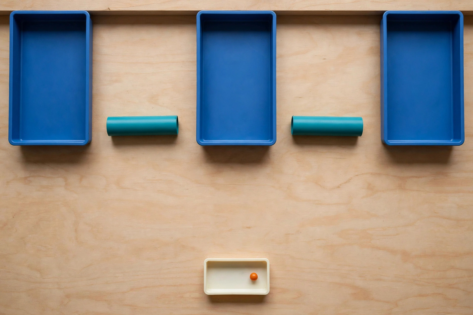 Three blue rectangular trays are arranged in a row on a wooden surface, with teal cylinders placed in the gaps between them.