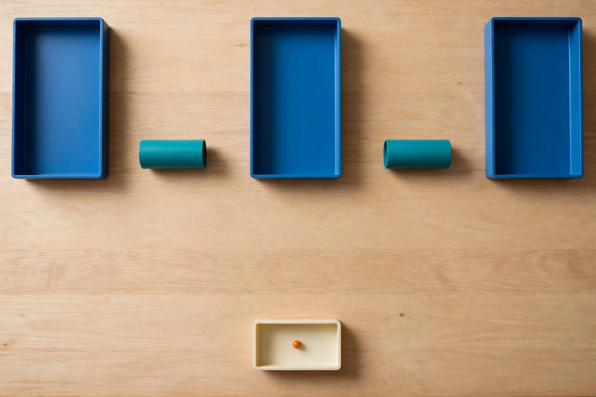 Three blue trays and two teal cylinders are arranged on a wooden surface, with an orange bead in a small ivory tray below.