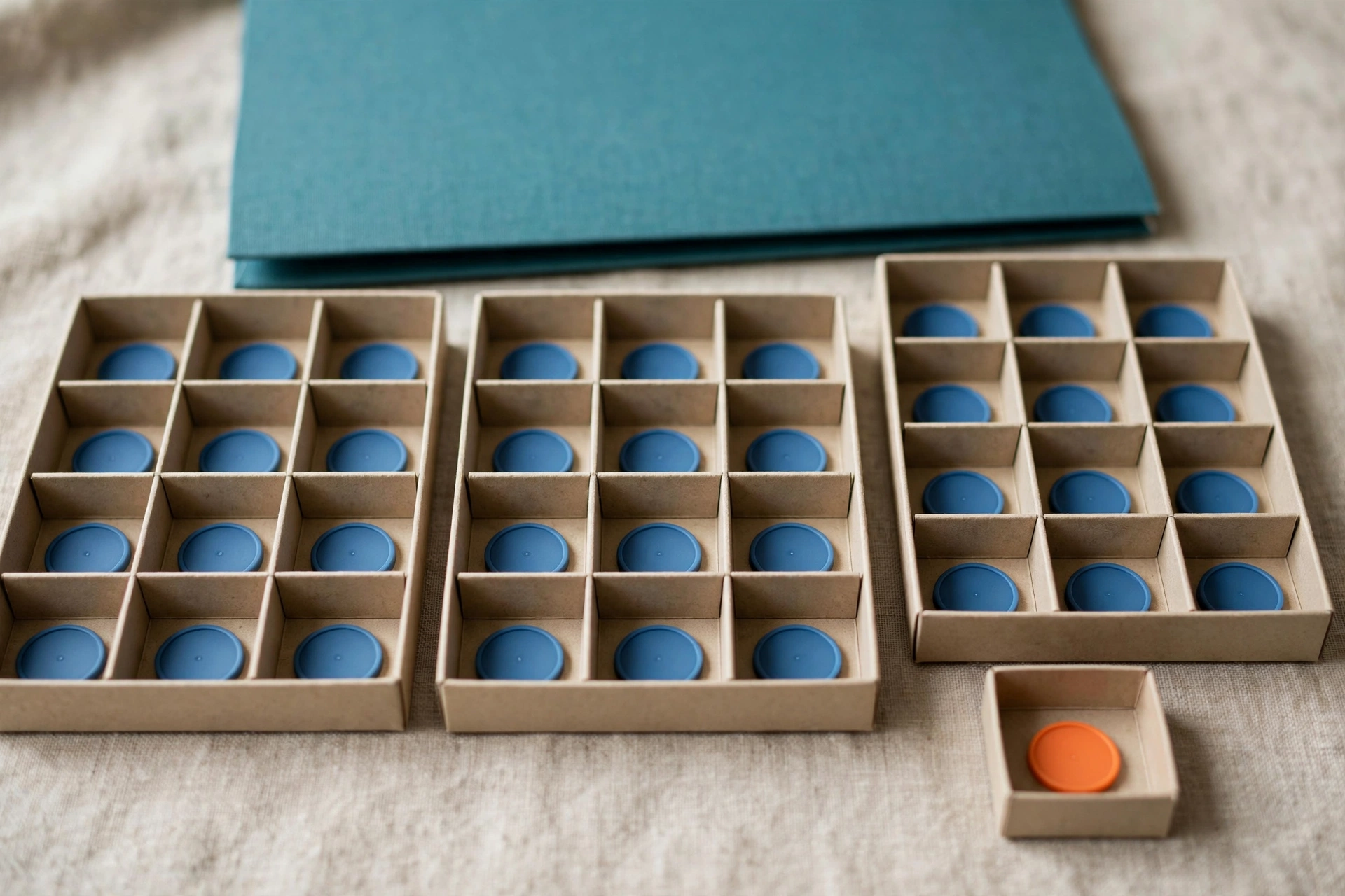 Blue tokens are distributed in sorting trays, with one orange token in a separate small tray, and a teal folder behind.