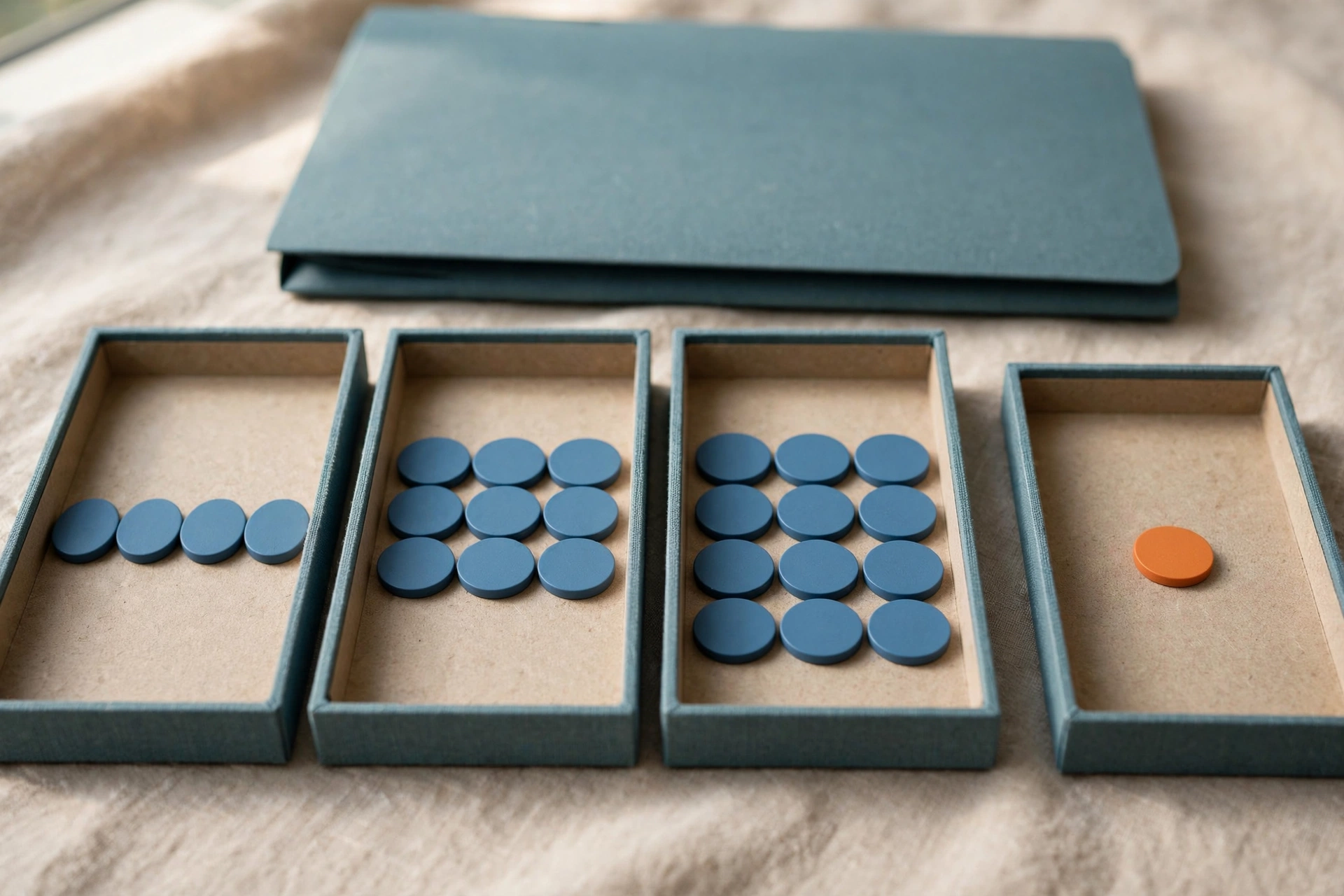 Four shallow office trays with blue tokens progress from left to right, with an orange token isolated in the fourth tray.