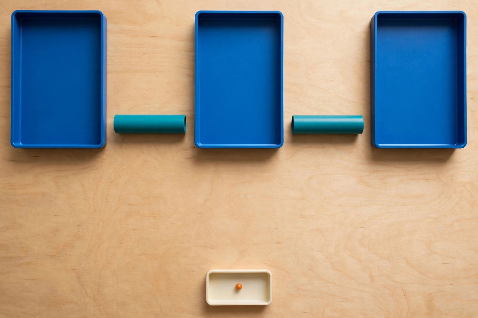 Three blue trays and two teal cylinders are arranged on a wooden surface, with a small ivory tray containing an orange bead below.
