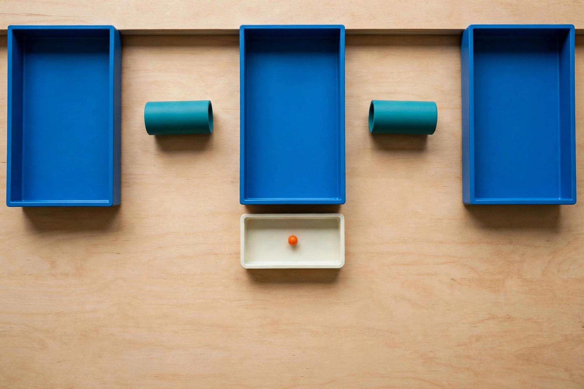 Three blue trays and two teal cylinders are arranged on a wooden surface, with an ivory tray containing an orange bead below.