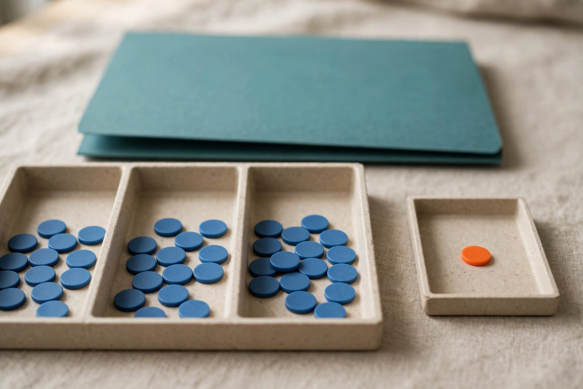 Blue tokens are distributed in three sections of a tray, with one orange token in a separate small tray, and a teal folder behind.
