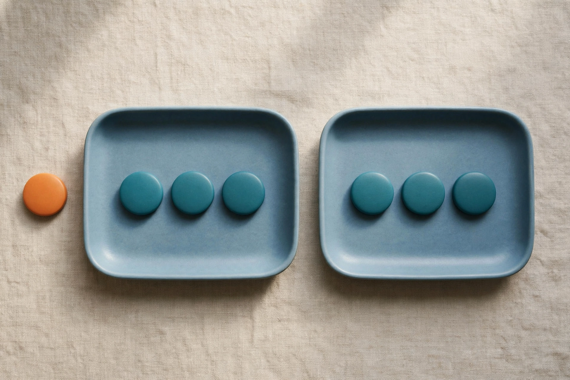 Two blue trays hold teal tokens, with an orange token placed beside one tray on a textured surface.