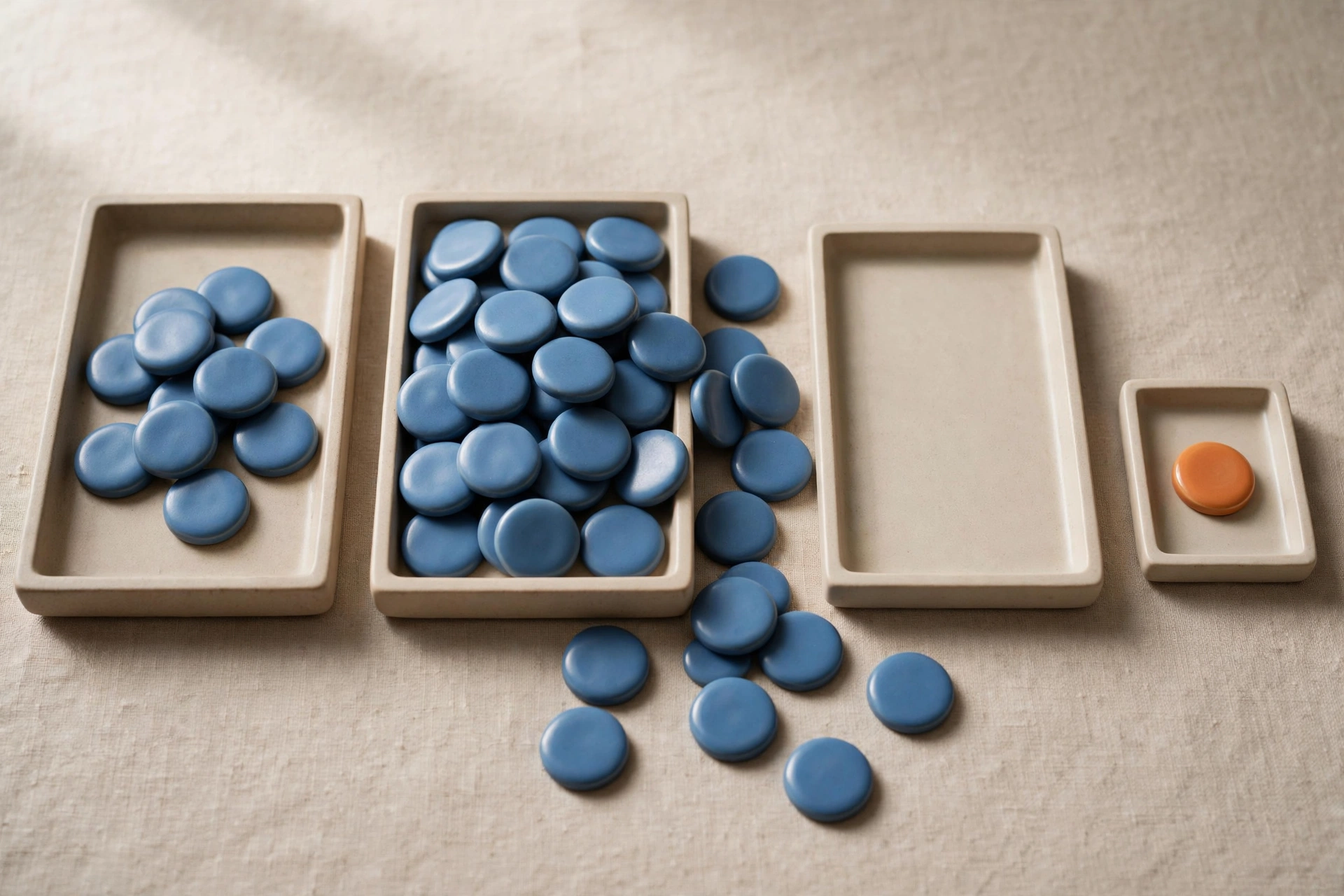 Three shallow trays hold blue tokens, with one tray empty and an isolated orange token in a small tray.