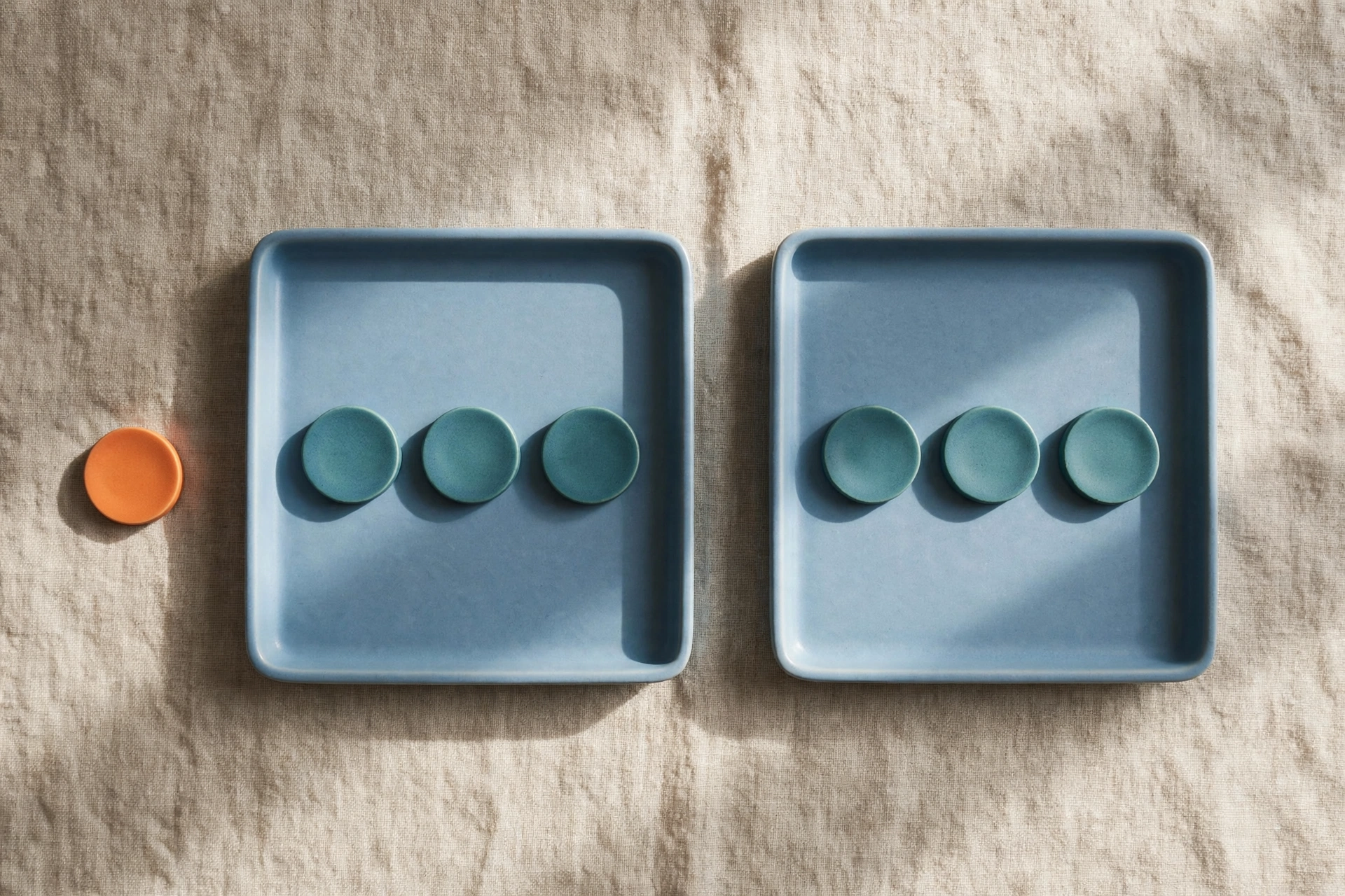 Two blue trays each hold three teal tokens, with a single orange token placed beside the left tray.