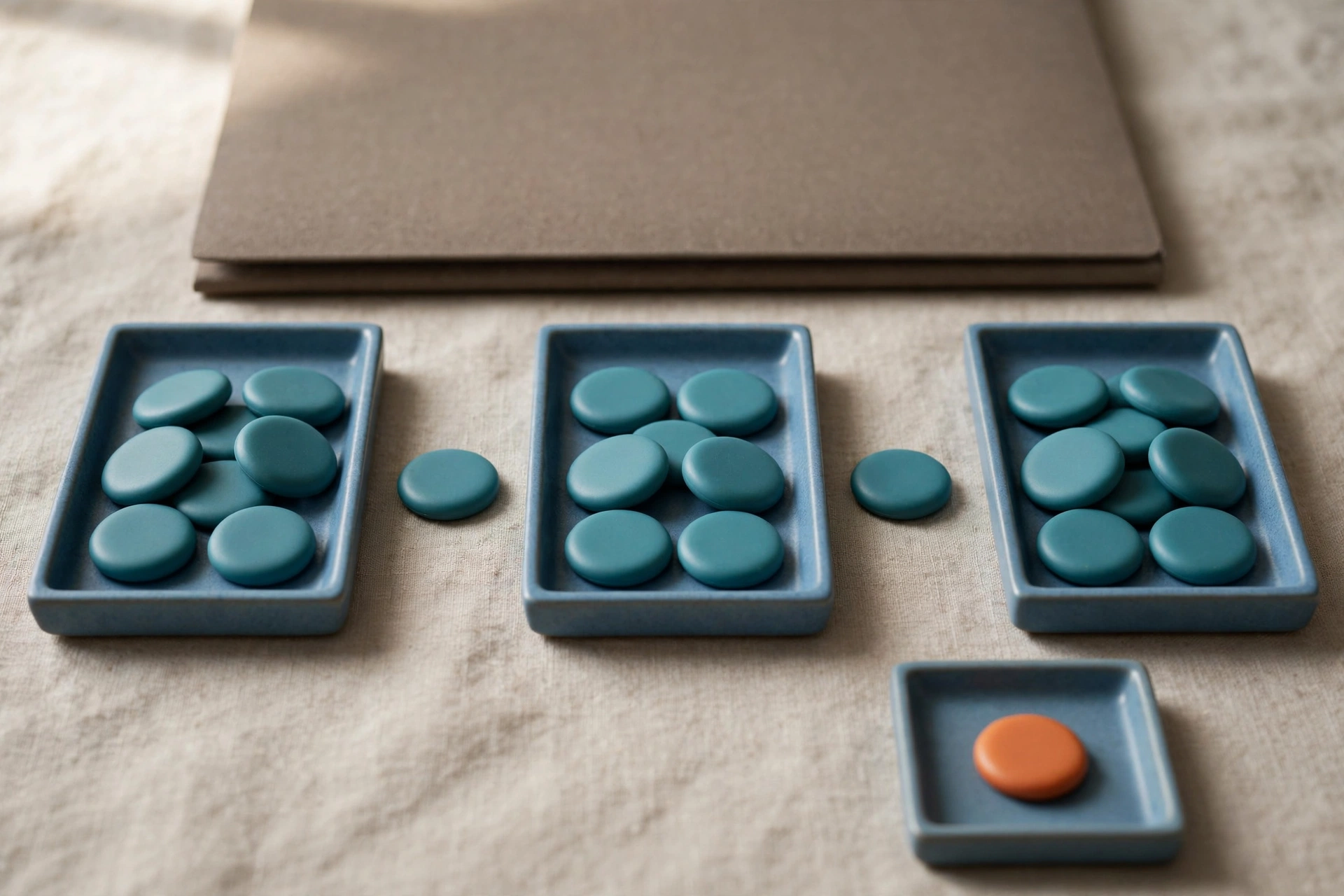 Three blue trays with teal tokens in a sequence and a separate tray with an orange token are arranged on a neutral cloth.