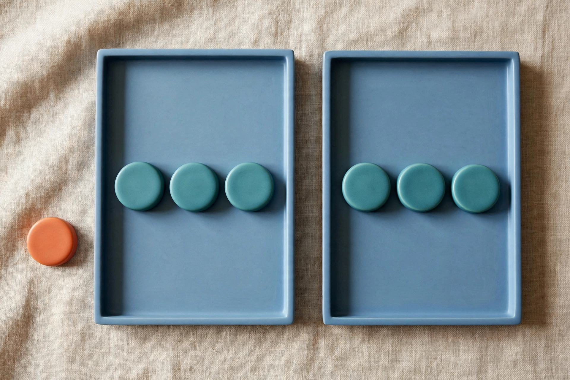 Two blue trays each hold three teal tokens, with a single orange token placed beside the left tray.