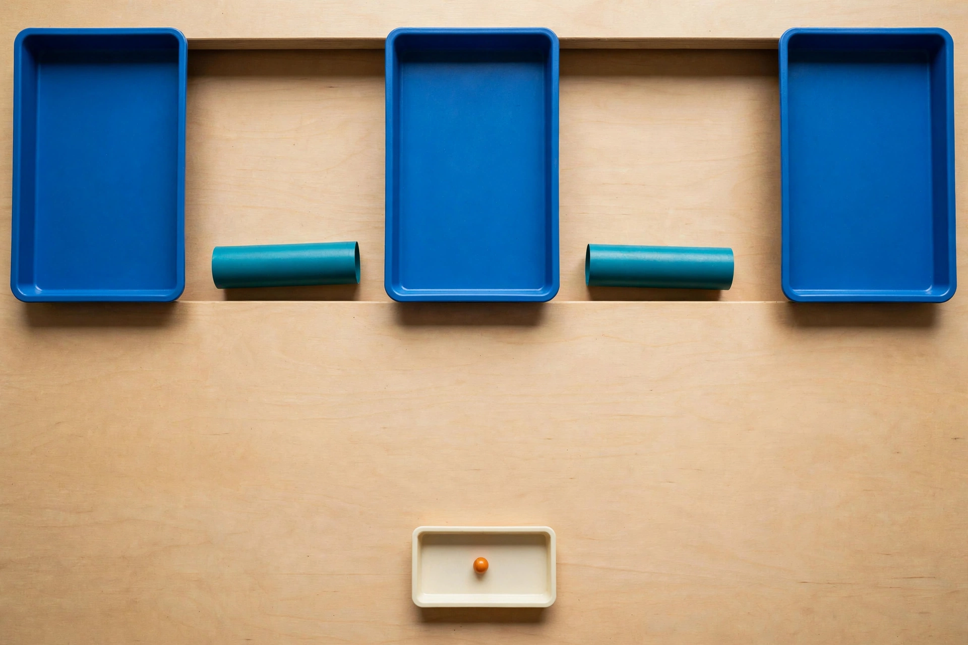 Three blue trays and two teal cylinders are arranged on a wooden surface, with a small ivory tray containing an orange bead below.