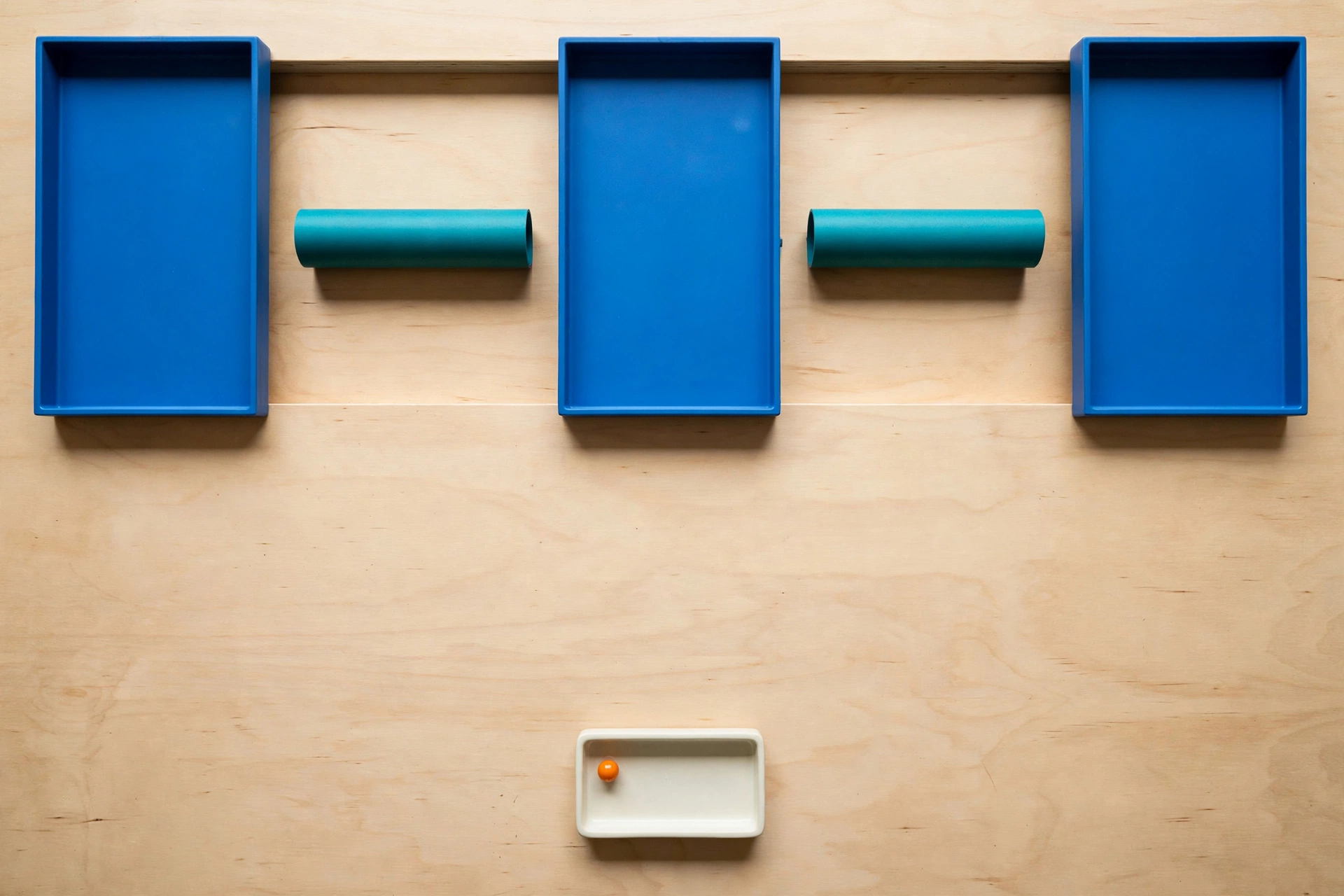 Three blue rectangular trays are arranged in a row with two teal cylinders in the gaps between them, and a small ivory tray with an orange bead below.