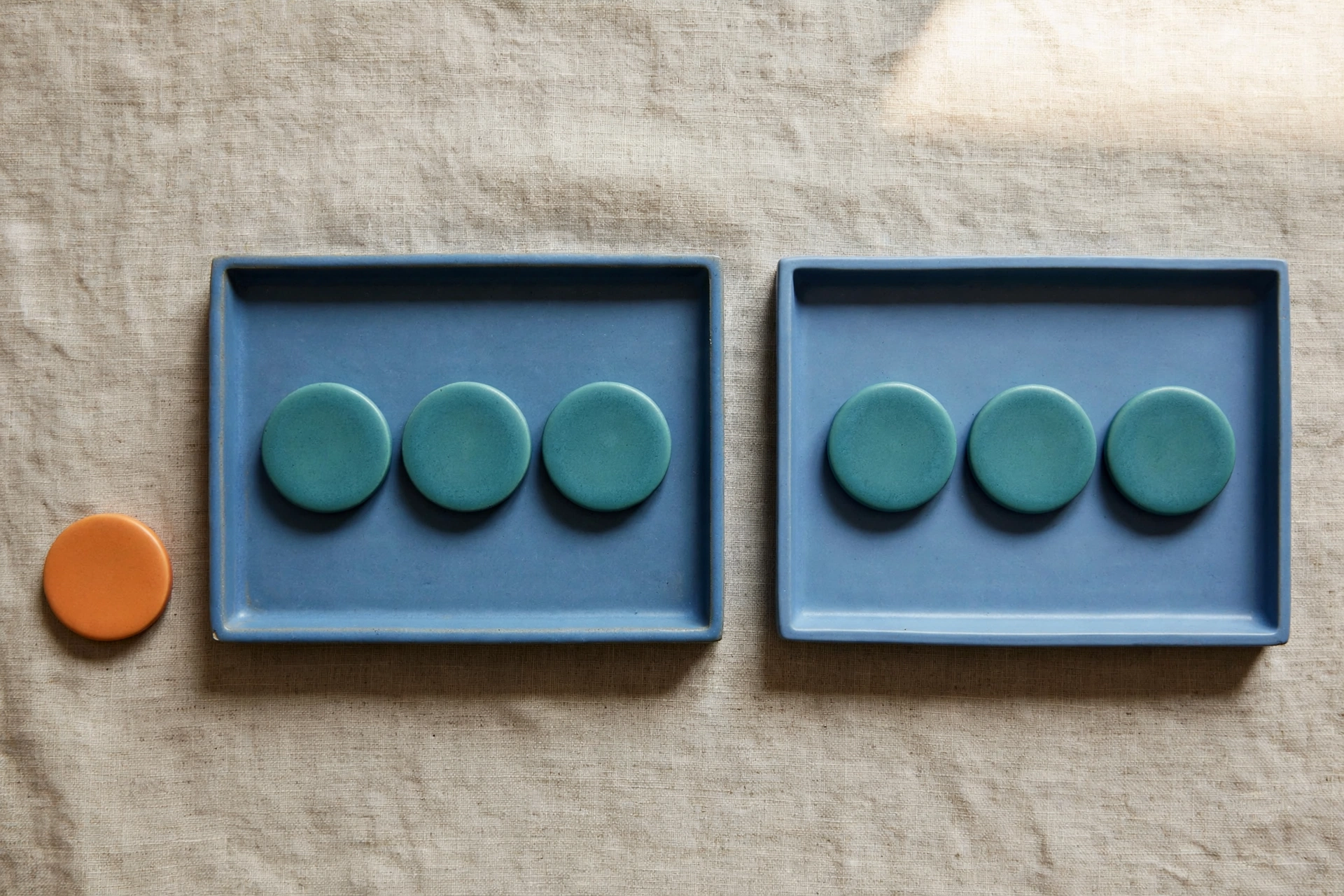 Two blue trays with teal tokens and an orange token sit on a textured surface.