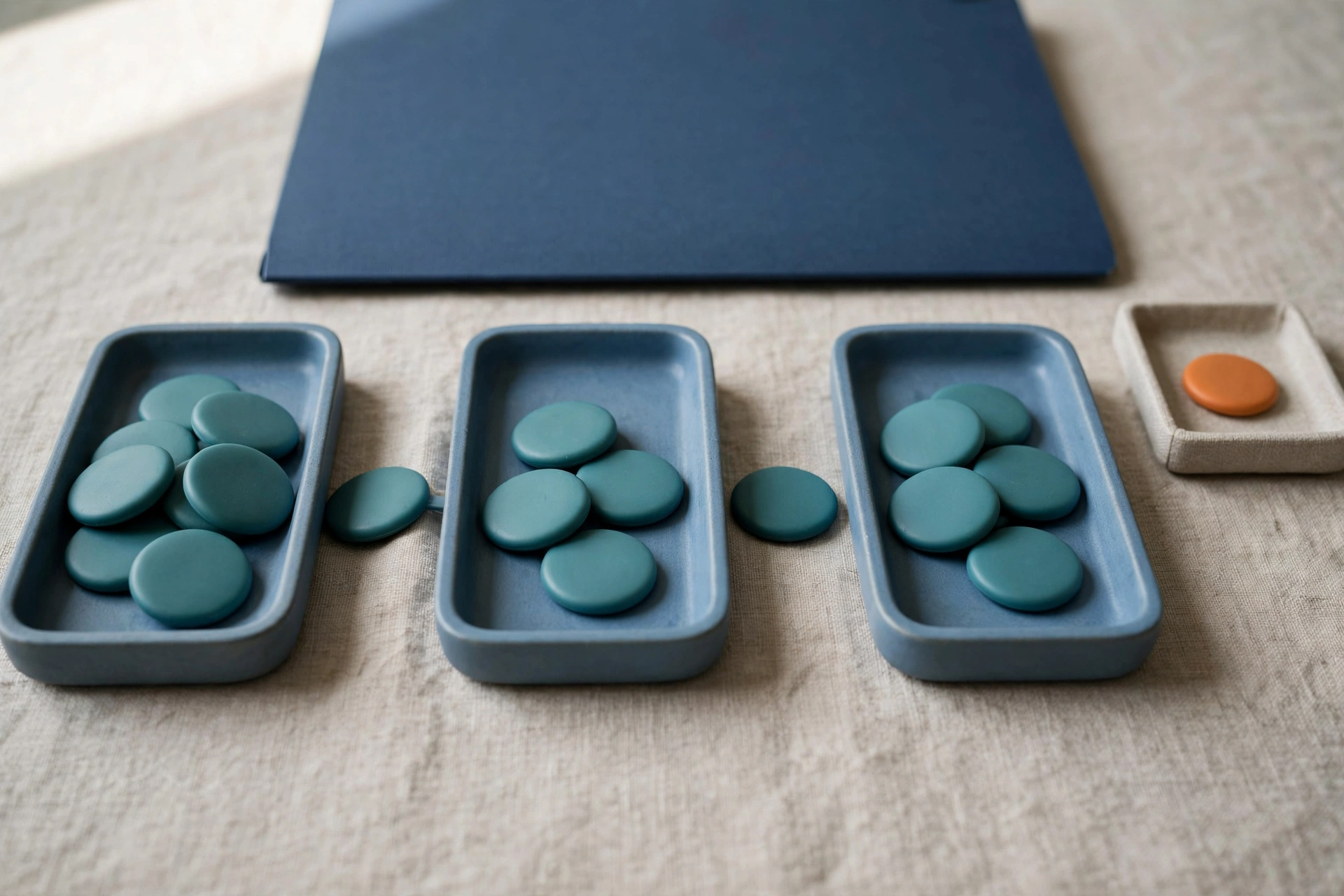 Three blue trays with teal tokens and one orange token in a separate tray are arranged on a textured surface with a blue folder behind.