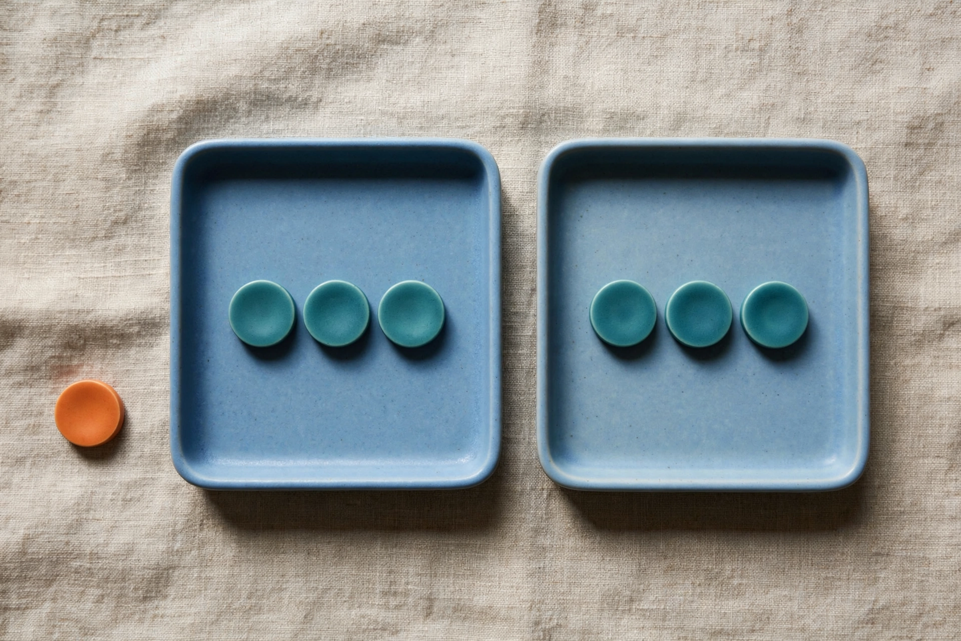 Two blue trays each hold three teal tokens, with a single orange token placed beside the left tray.