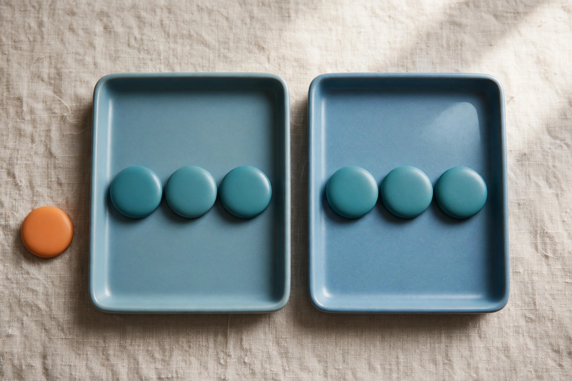 Two blue trays hold rows of teal tokens, with an orange token placed beside one tray on a textured surface.