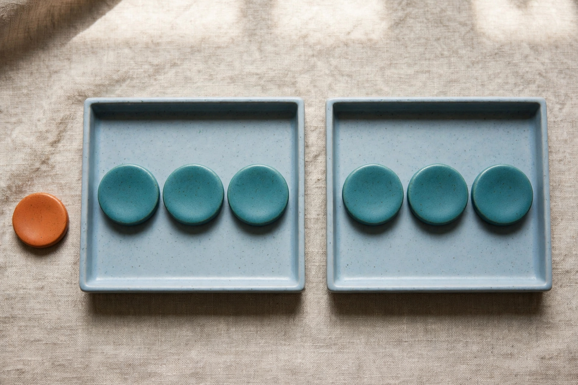 Two blue trays hold teal tokens, with an orange token placed beside one tray on a textured surface.