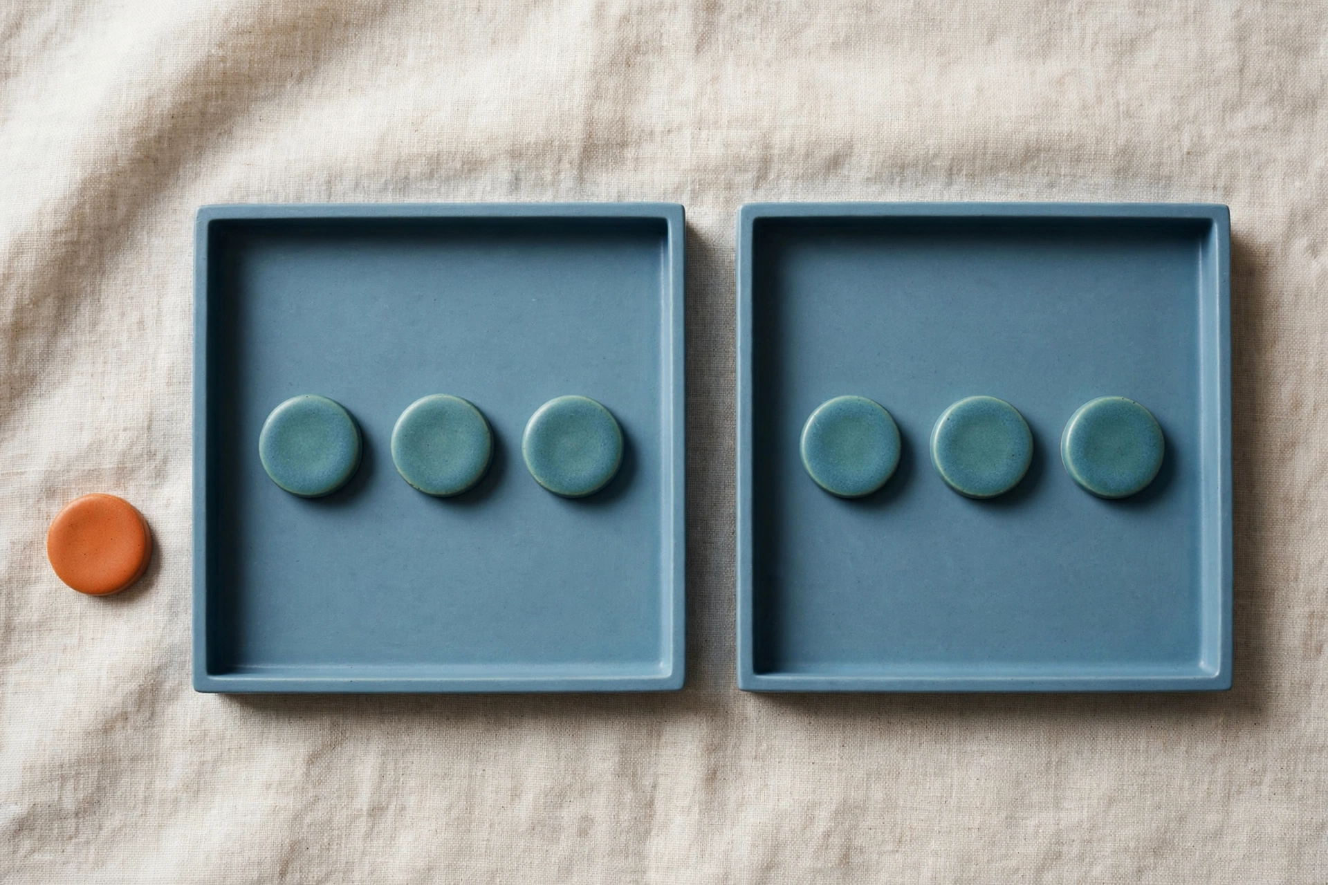 Two blue trays each hold three teal tokens, with a single orange token placed beside the left tray.