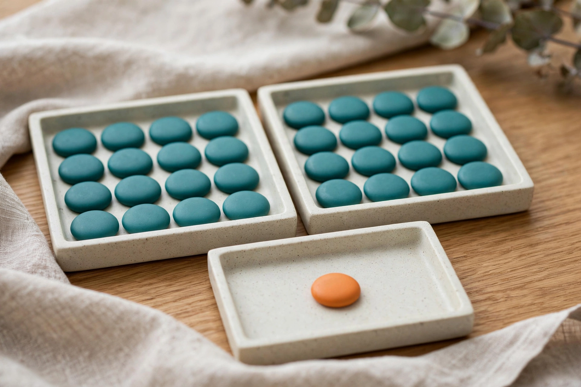 Two trays of teal tokens and one tray with a single orange token are arranged on a wooden surface with a cloth.