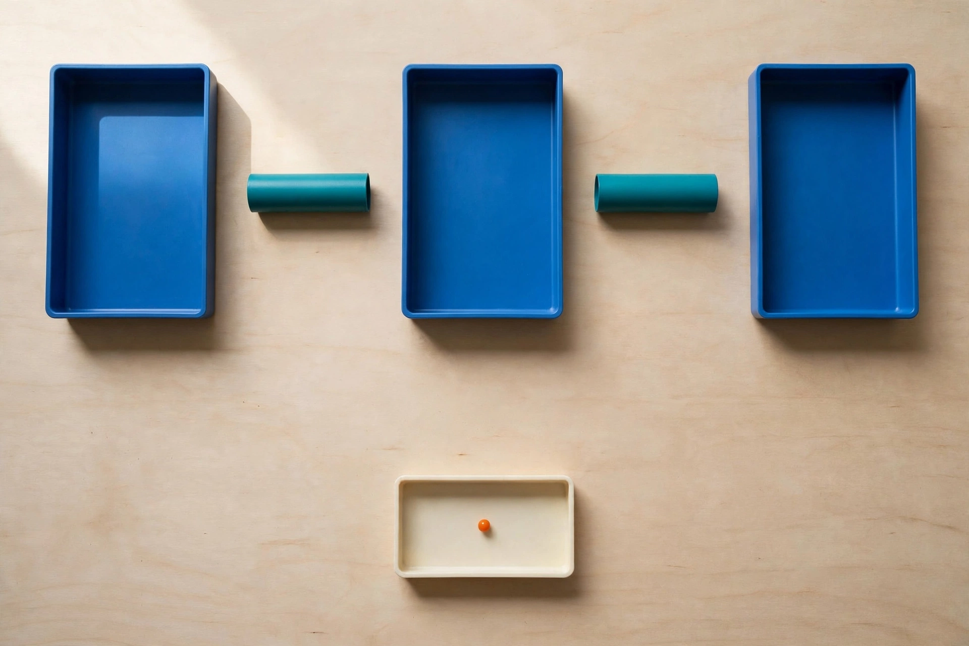 Three blue trays and two teal cylinders are arranged on a wooden surface, with a small orange bead in a lower ivory tray.