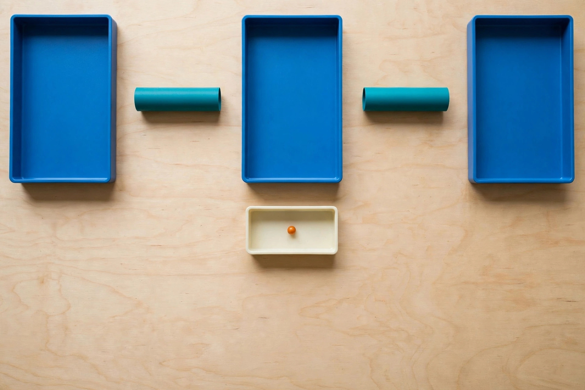 Three blue trays and two teal cylinders are arranged on a wooden surface, with an orange bead in a small ivory tray below.