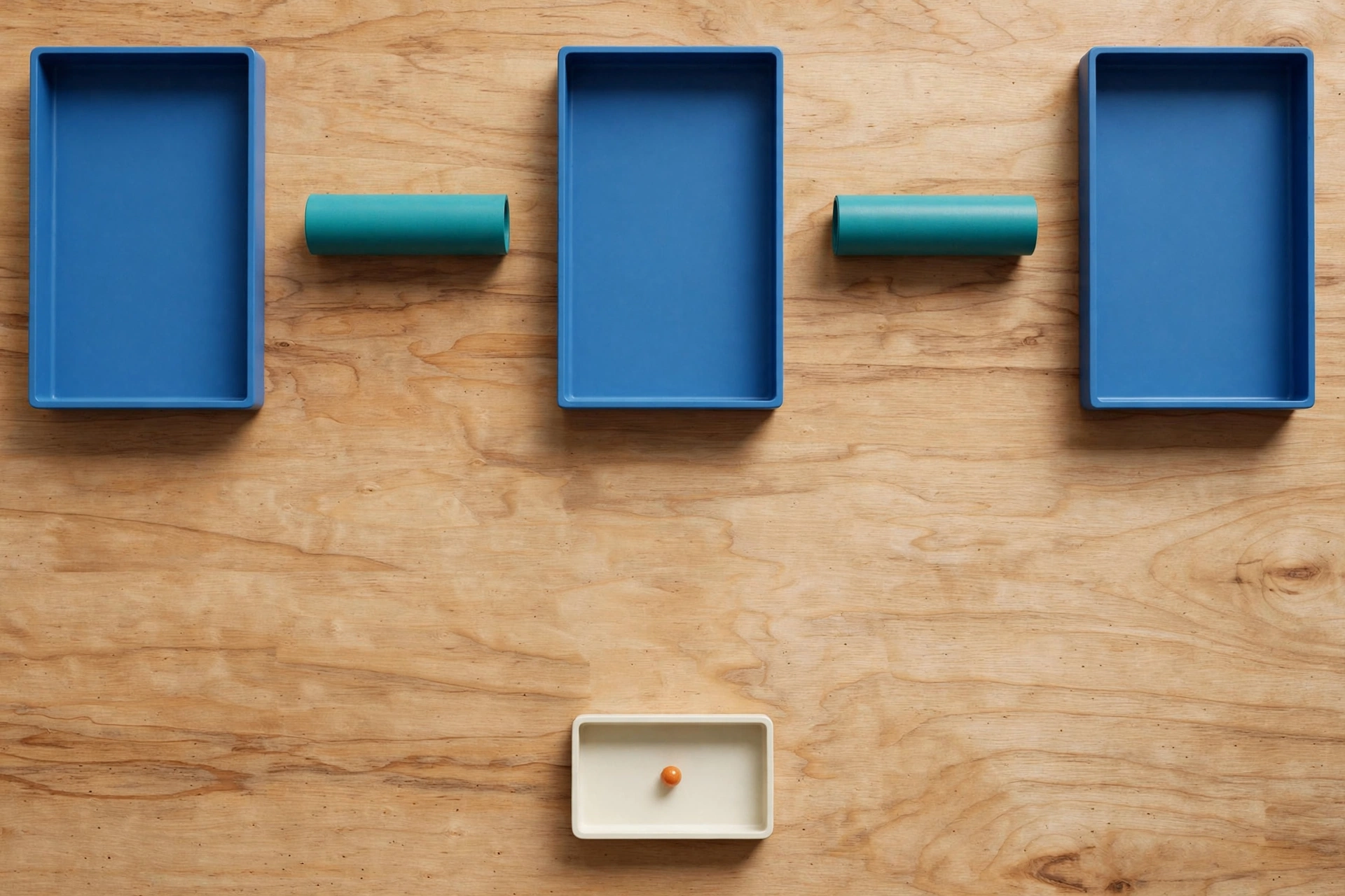 Three blue trays and two teal cylinders are arranged on a wooden surface, with an orange bead in a lower ivory tray.