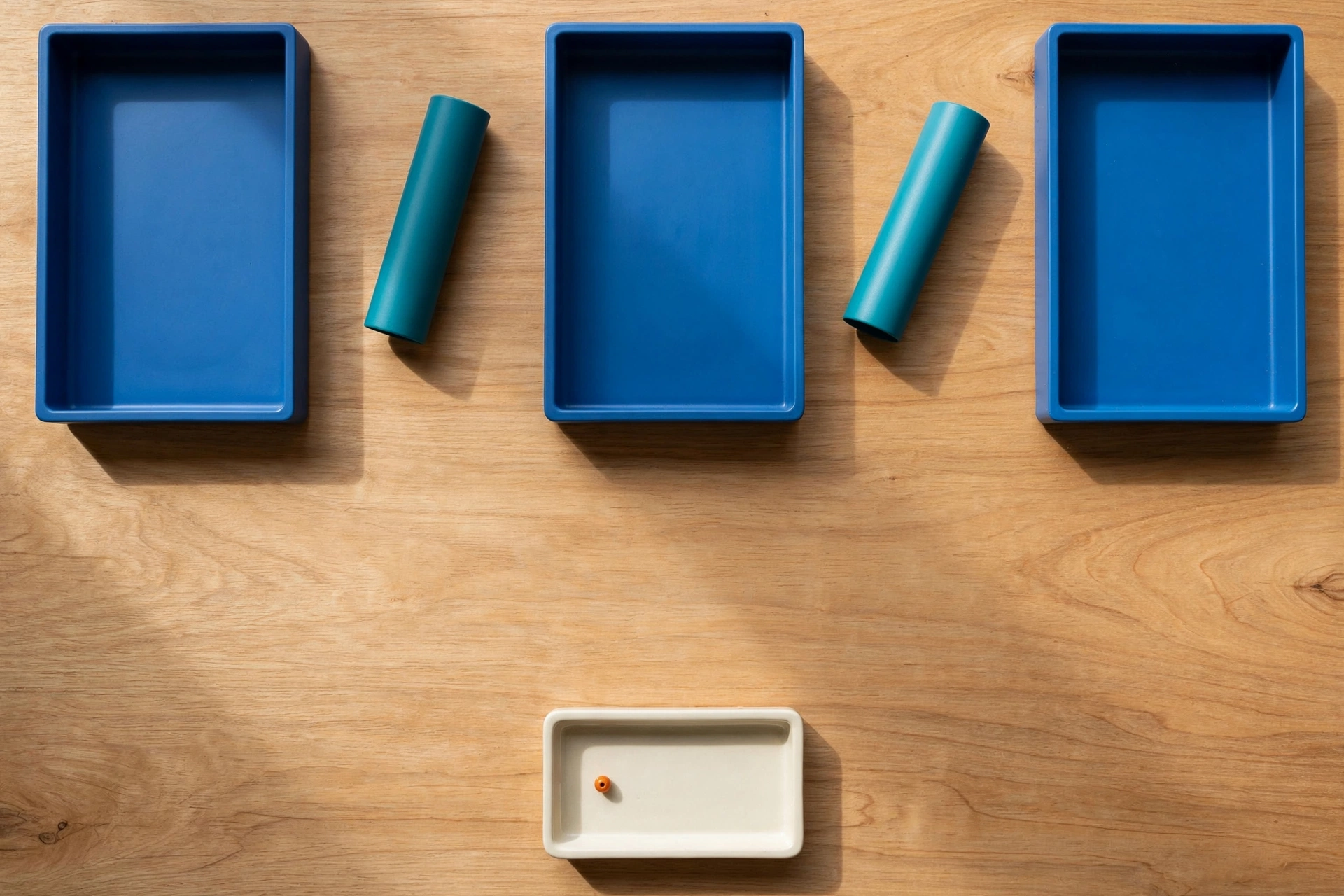 Three blue rectangular trays are arranged in a row on a wooden surface, with teal cylinders placed in the gaps between them.