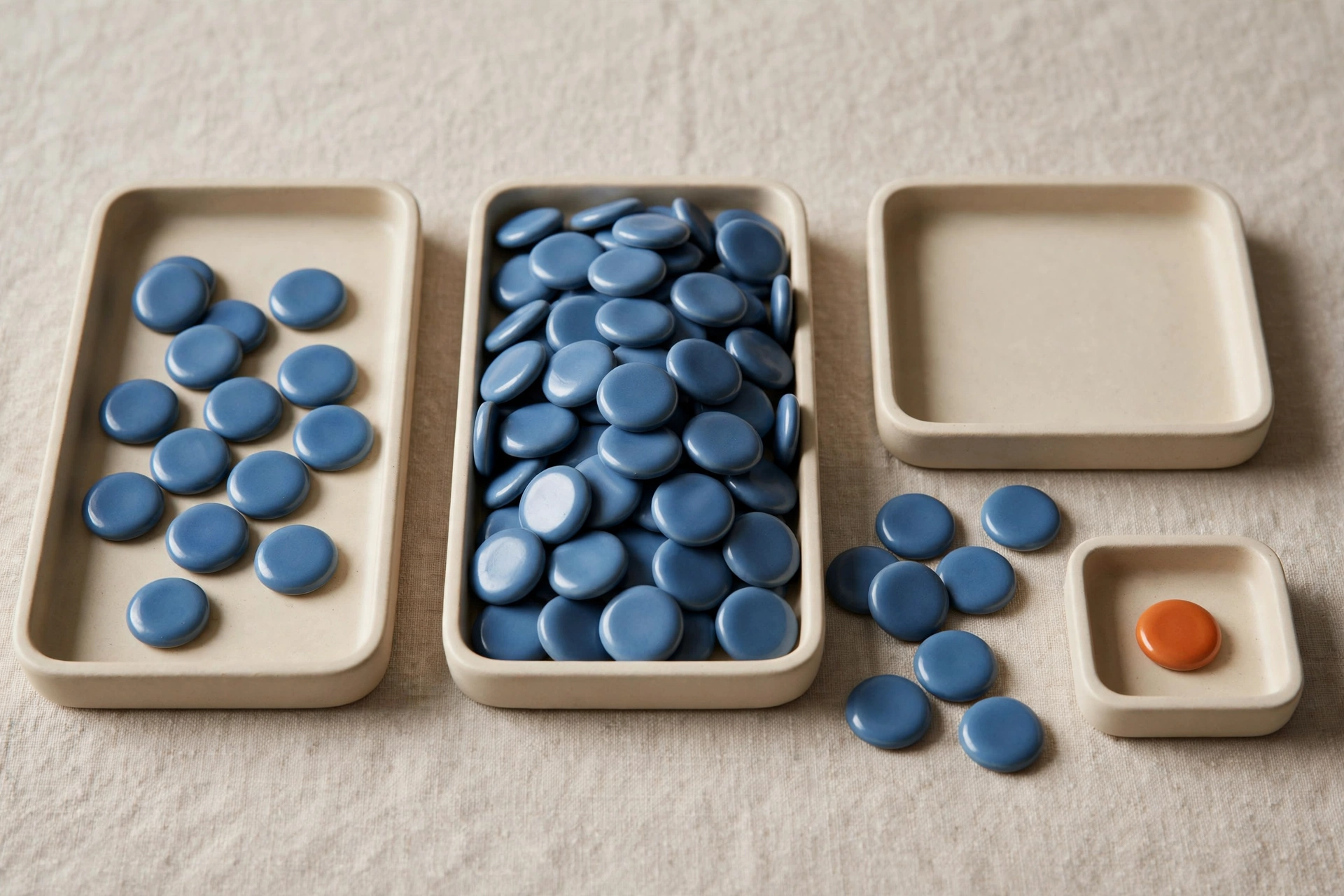 Three shallow trays hold varying amounts of blue tokens, with one tray empty, and a small tray holds a single orange token.