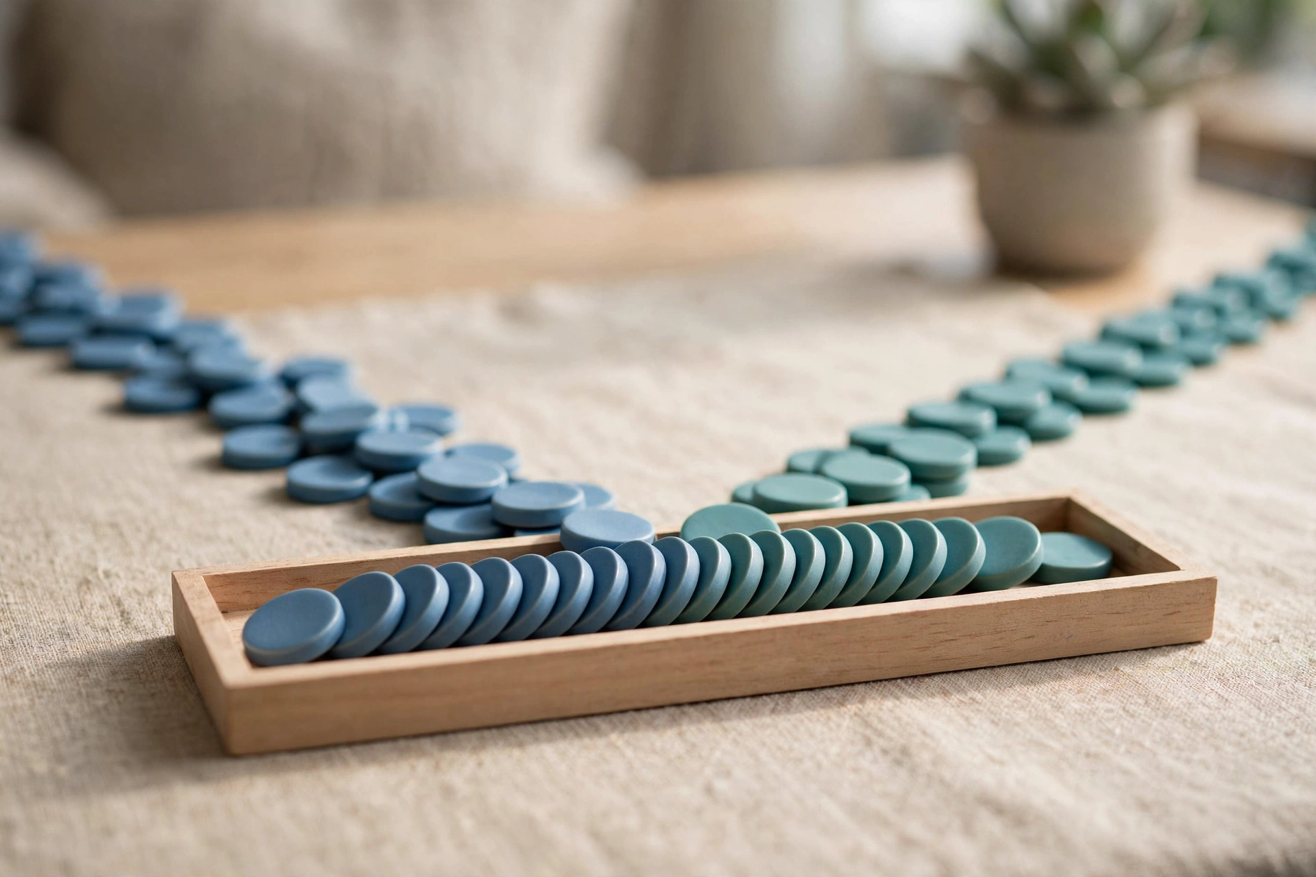Two streams of blue and teal ceramic tokens converge into a single ordered row within a shallow wooden tray on a textured surface.