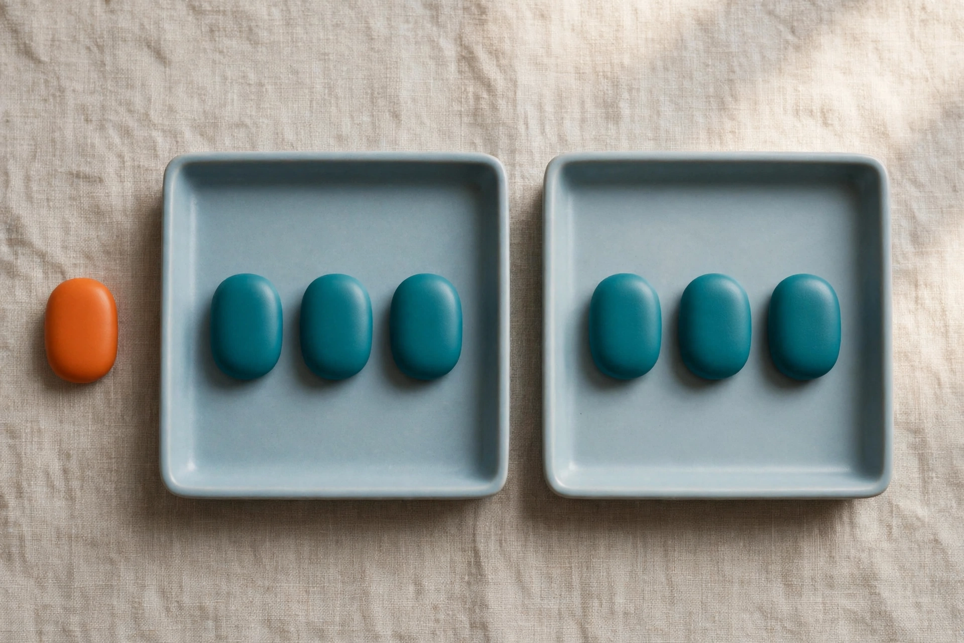 Two blue trays hold teal tokens, with an orange token placed beside one tray on a textured surface.