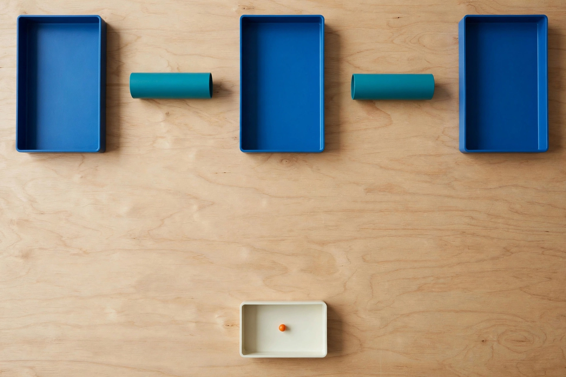 Three blue trays and two teal cylinders are arranged on a wooden surface, with one orange bead in a lower ivory tray.