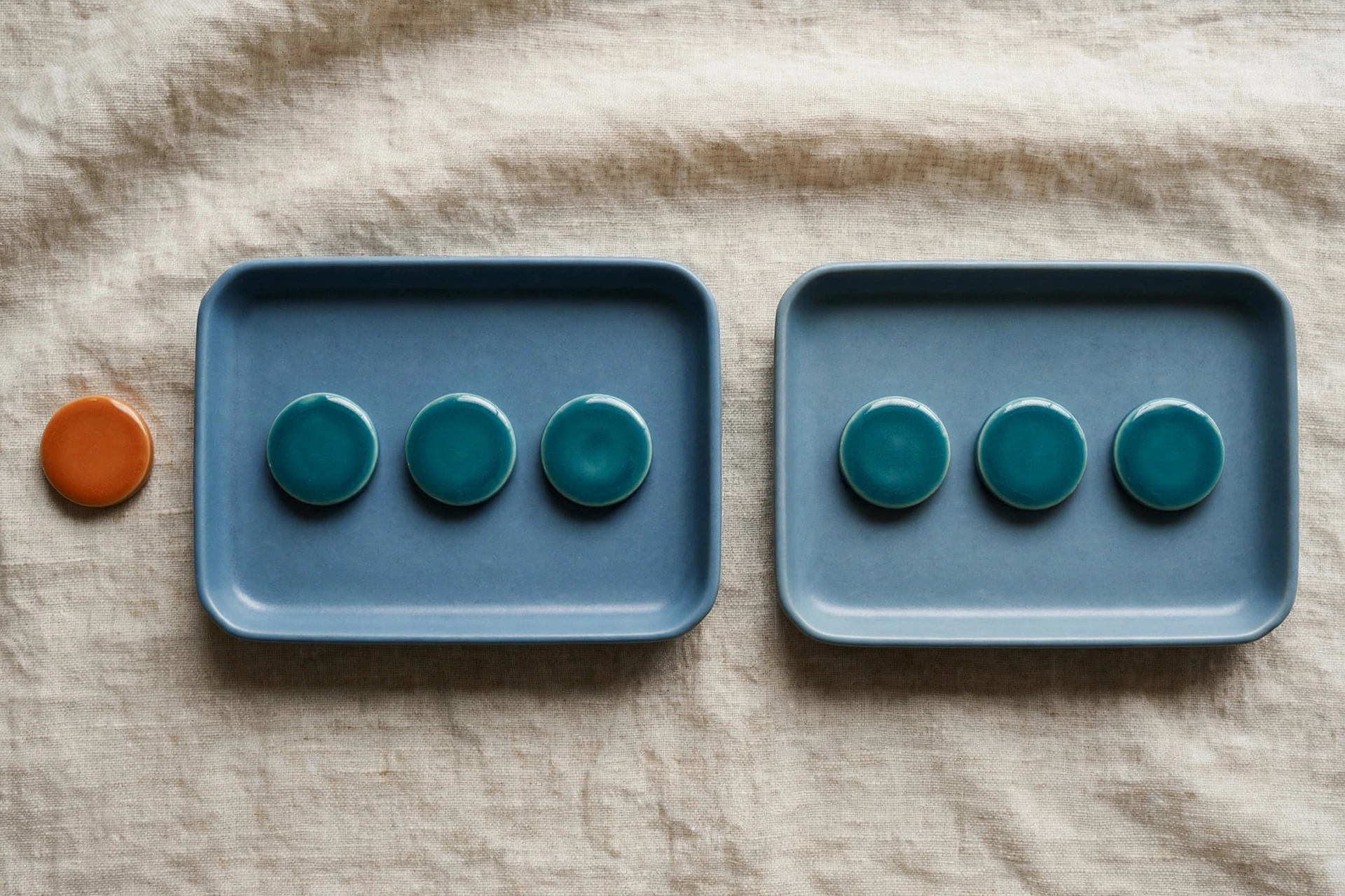 Two blue trays with teal tokens and an orange token beside the left tray on a textured surface.