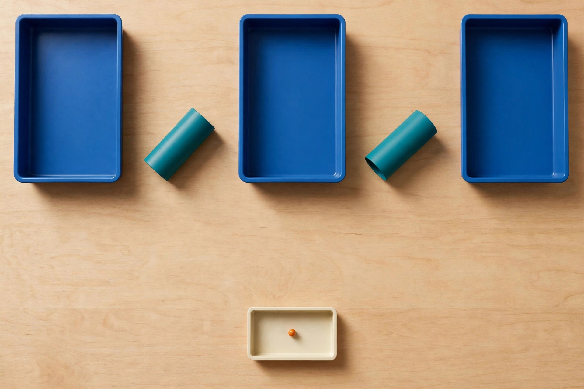 Three blue trays and two teal cylinders are arranged on a wooden surface, with a small orange bead in a separate ivory tray below.
