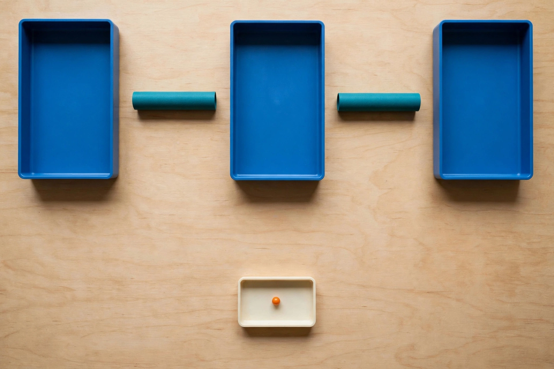 Three blue rectangular trays are arranged in a row on a wooden surface, with teal cylinders placed in the gaps between them.