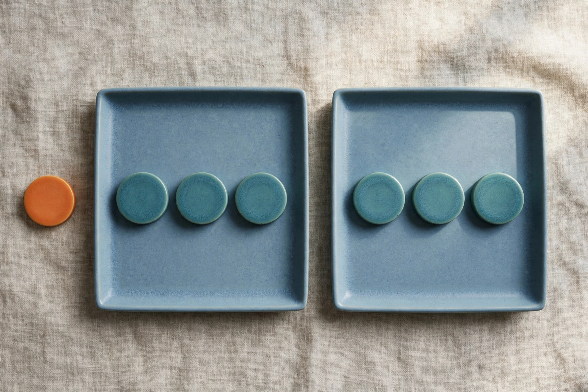 Two blue trays each hold three teal tokens, with a single orange token placed beside the left tray on a textured surface.