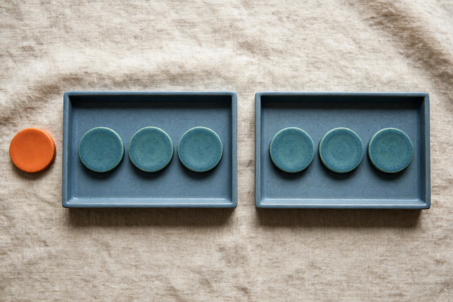 Two blue trays with teal tokens and an orange token beside one tray on a textured surface.