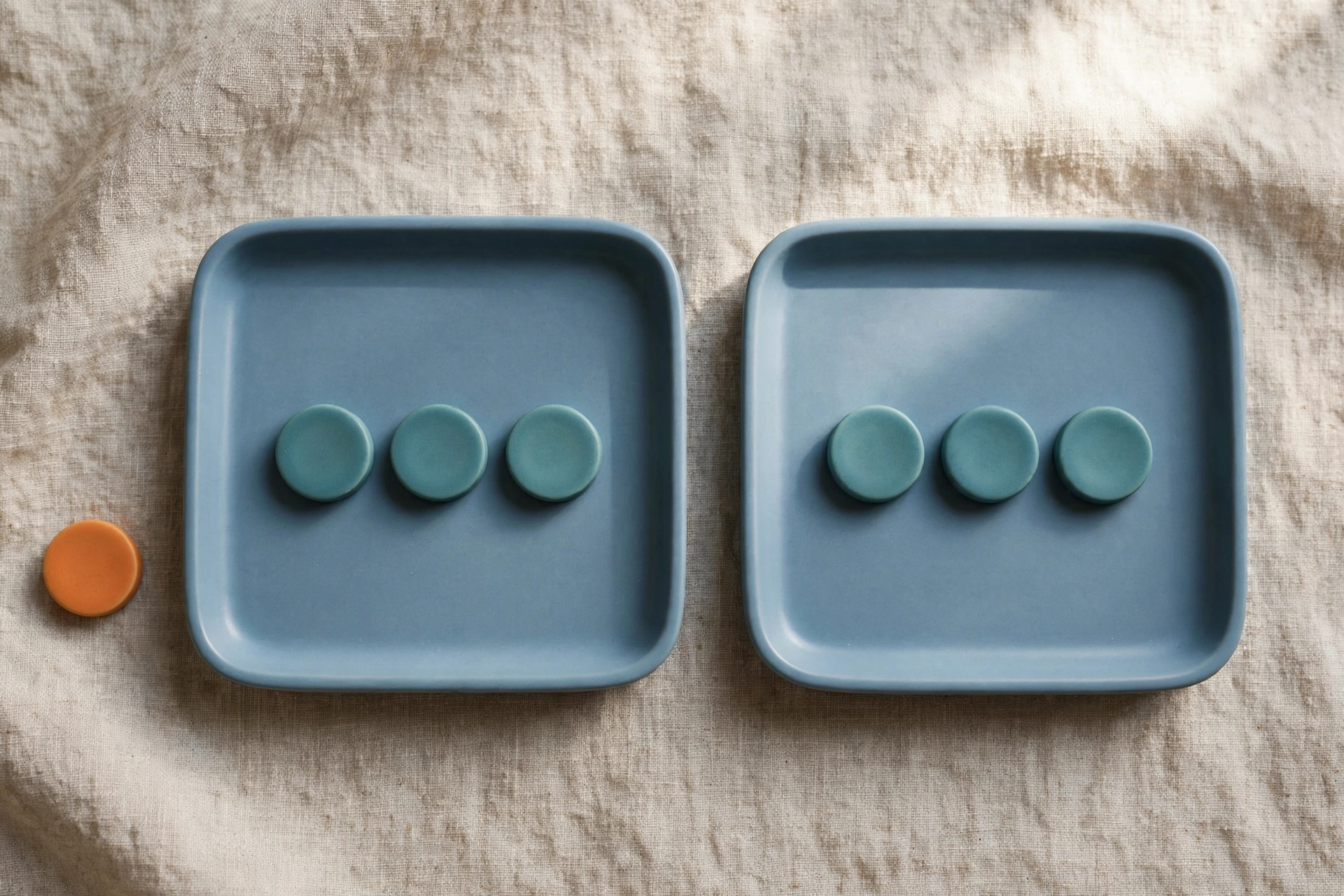 Two blue trays each hold three teal tokens, with a single orange token placed beside the left tray on a textured surface.