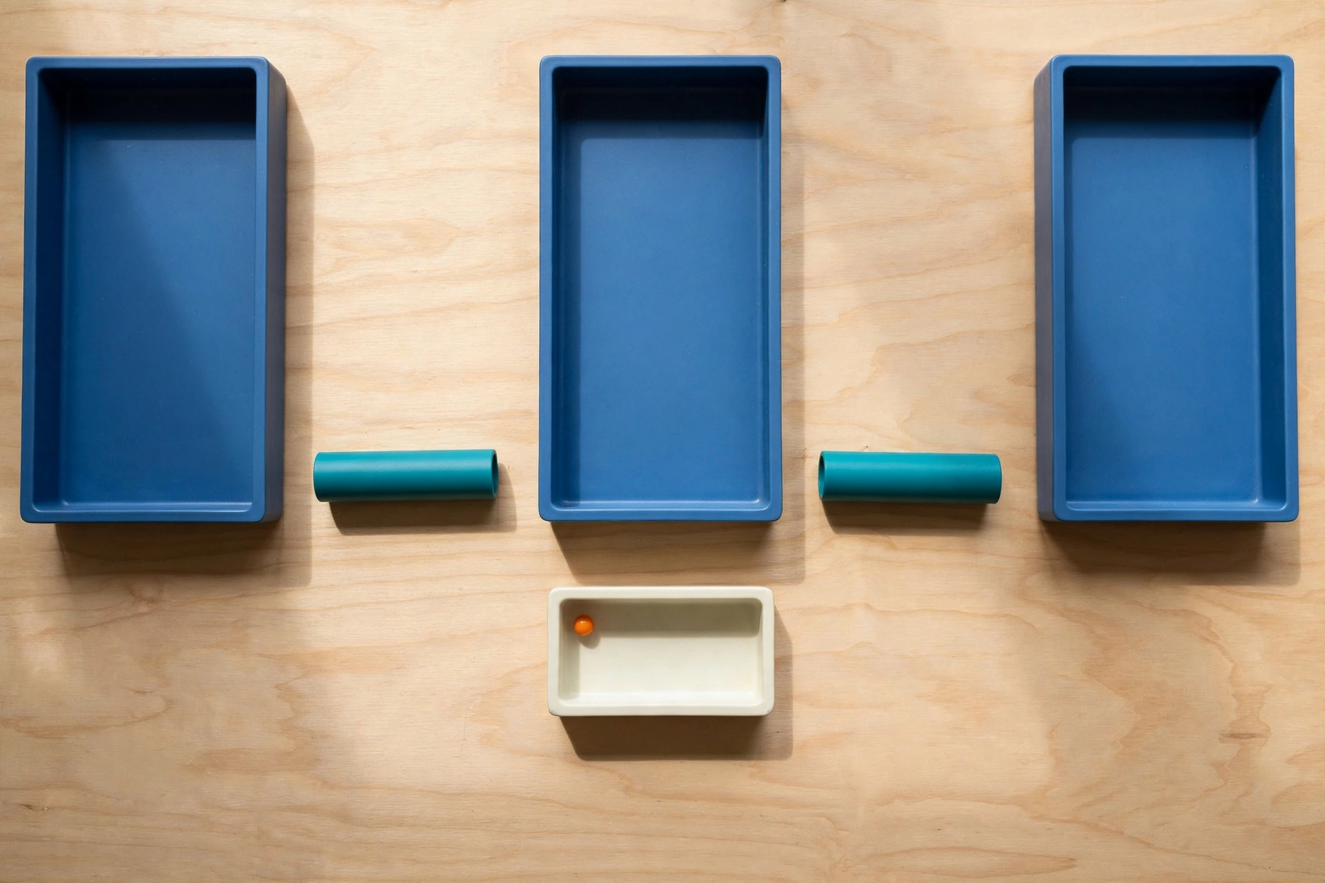 Three blue rectangular trays are arranged in a row on a wooden surface, with teal cylinders placed in the gaps between them.