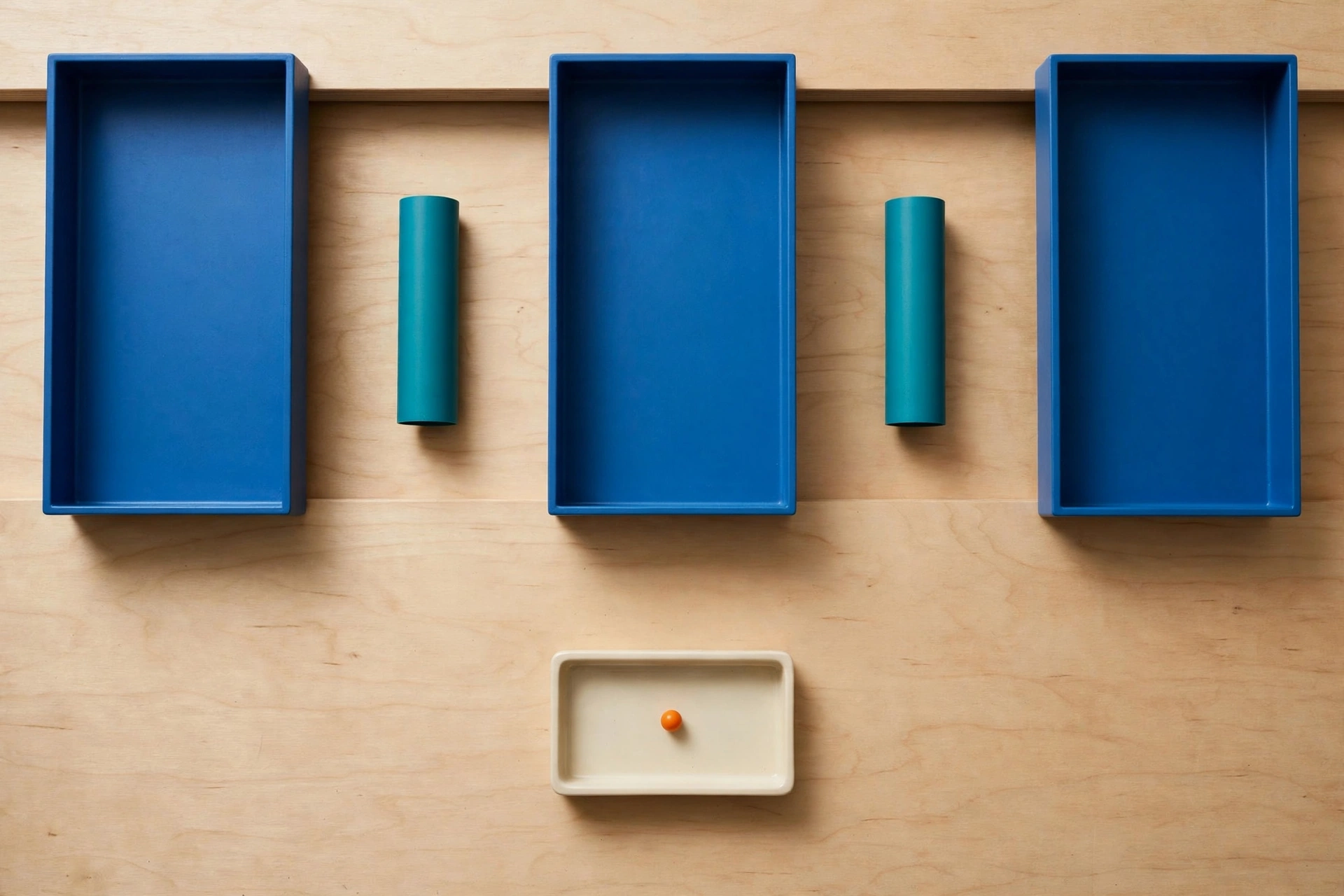 Three blue trays and two teal cylinders are arranged on a wooden surface, with a small ivory tray containing an orange bead below.