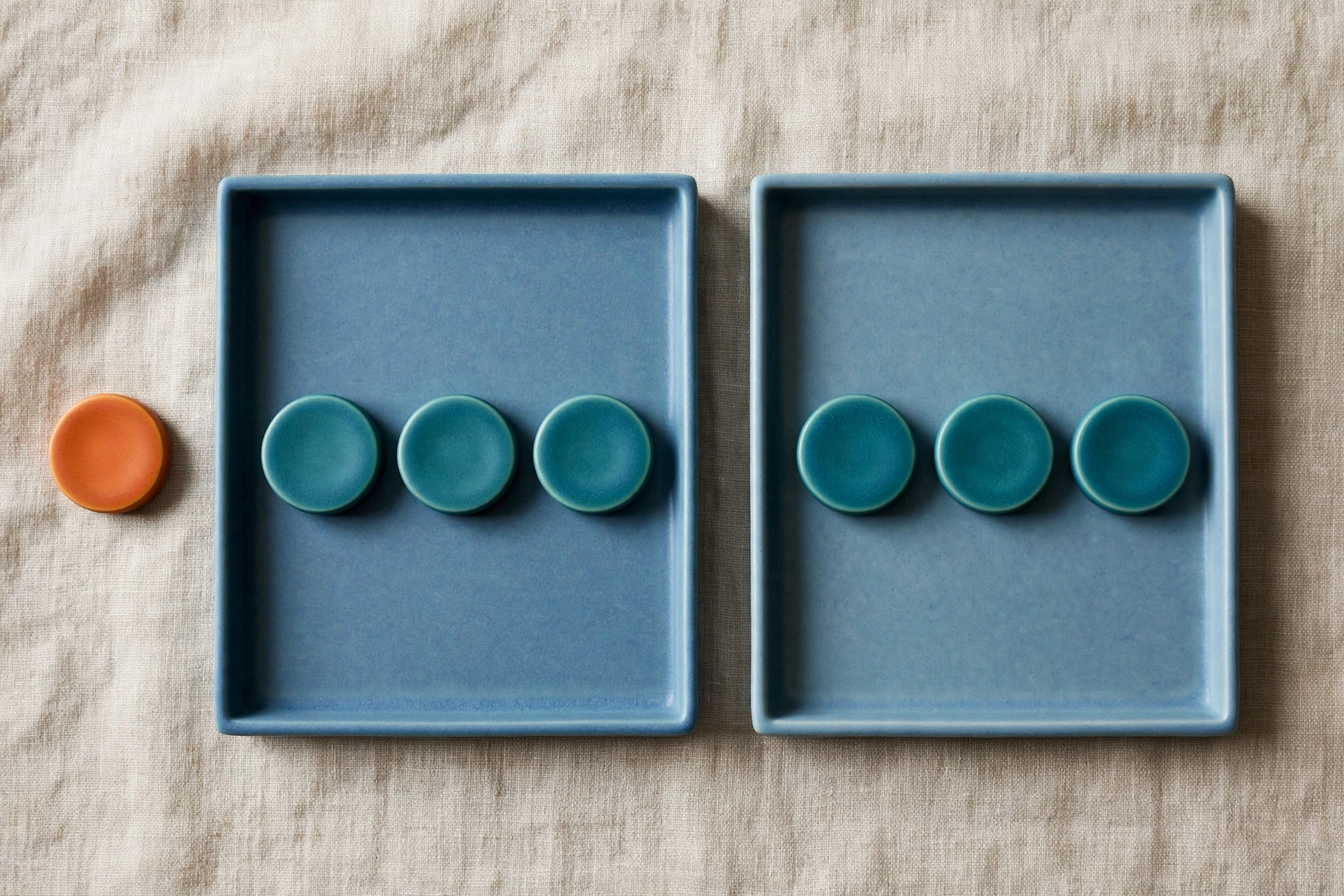 Two blue trays each hold three teal tokens, with one orange token placed beside the left tray.