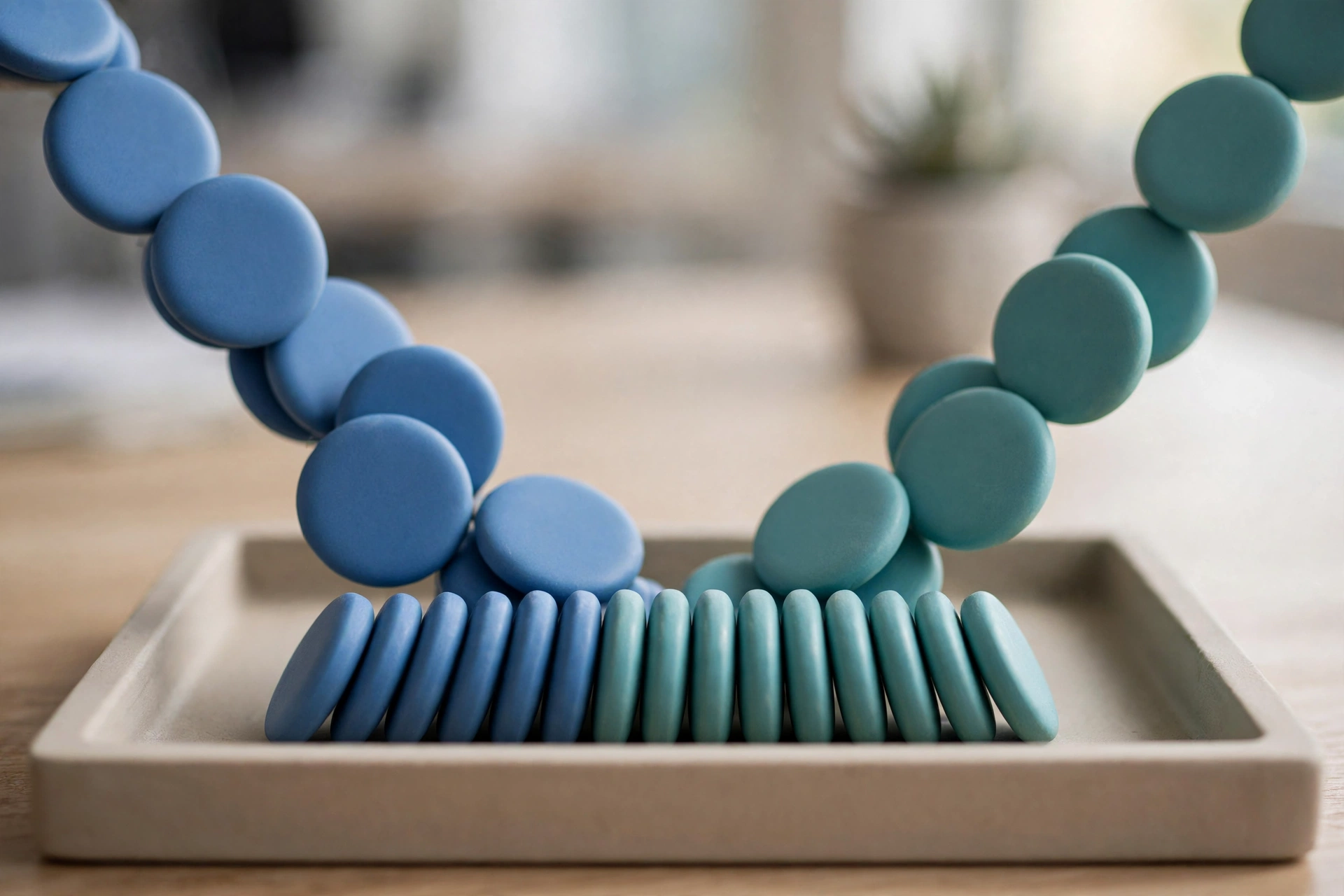 Two strands of blue and teal circular tokens converge into a single organized row within a shallow tray.