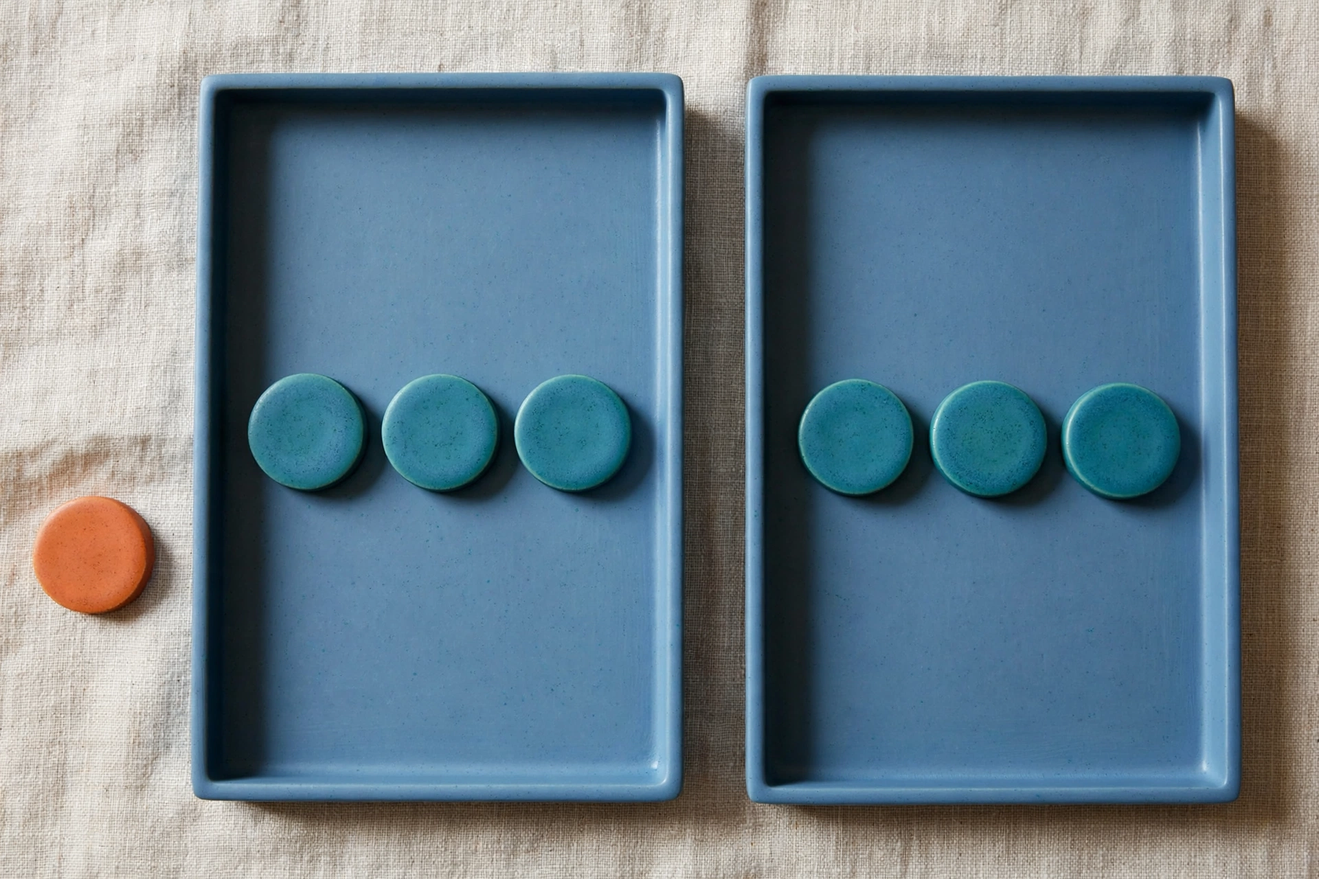 Two blue trays each hold three teal tokens, with one orange token placed beside the left tray.