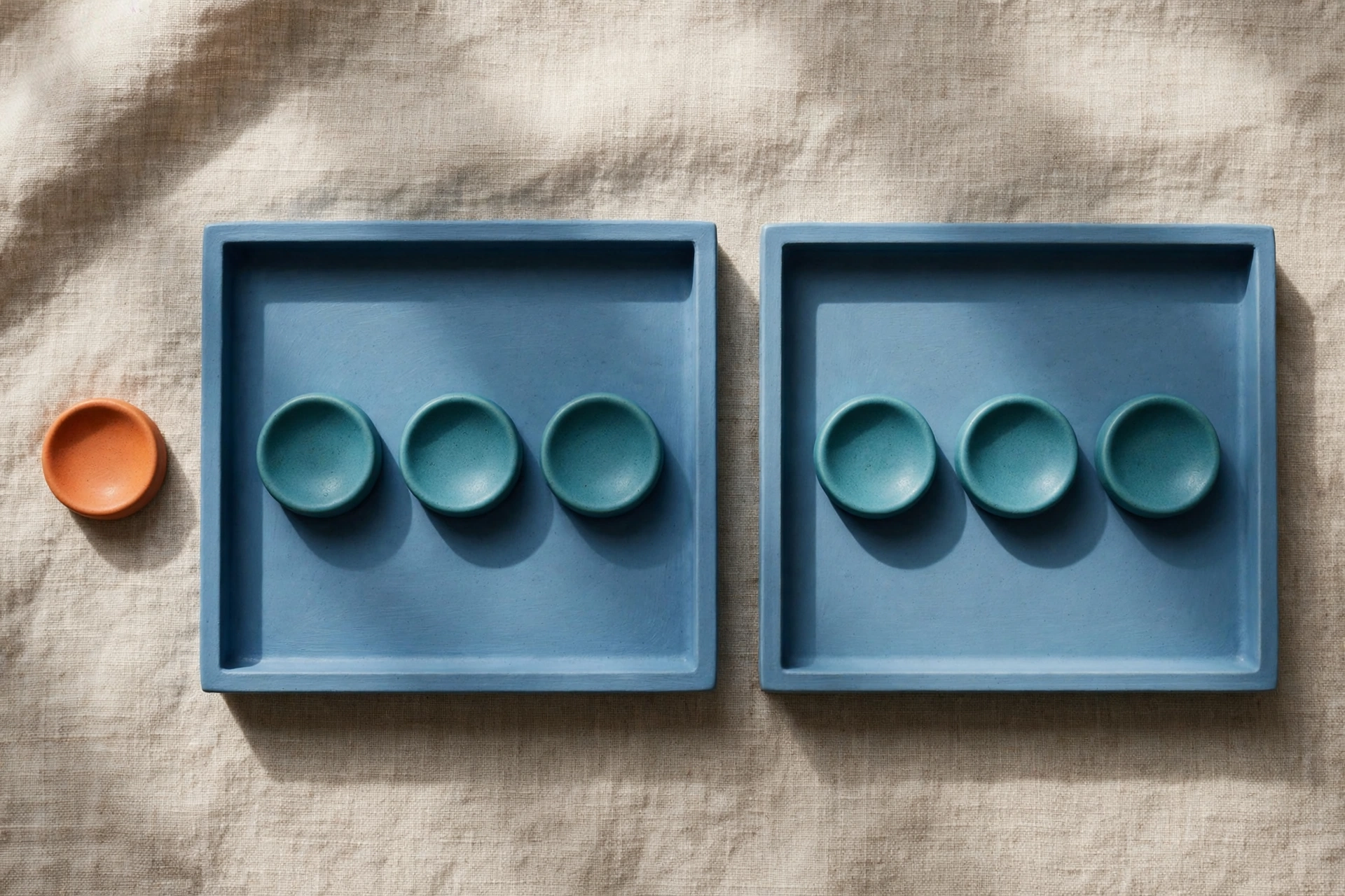 Two blue trays with teal tokens and an orange token beside one tray on a textured surface.
