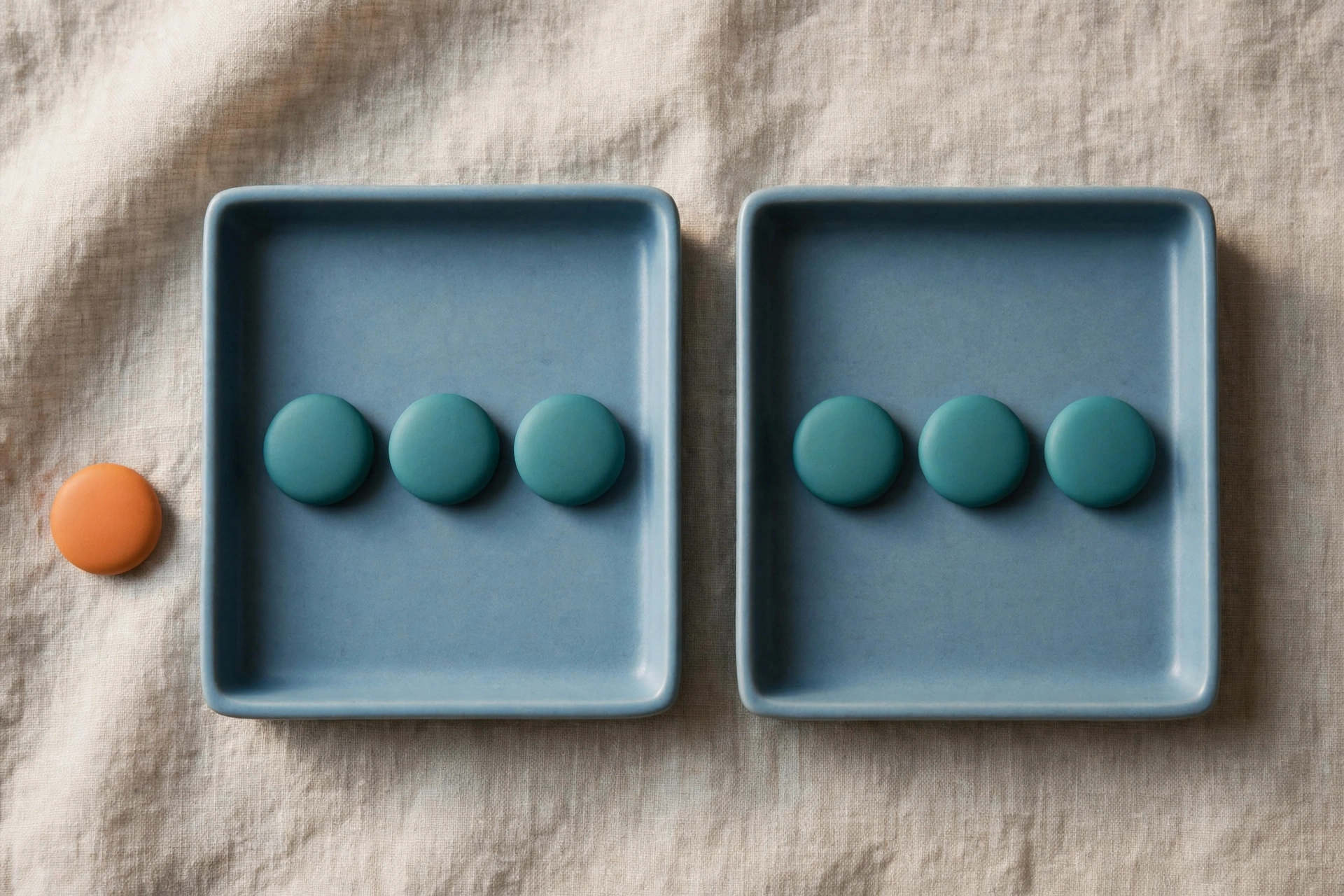 Two blue trays hold rows of teal tokens, with an orange token placed beside one tray on a textured surface.