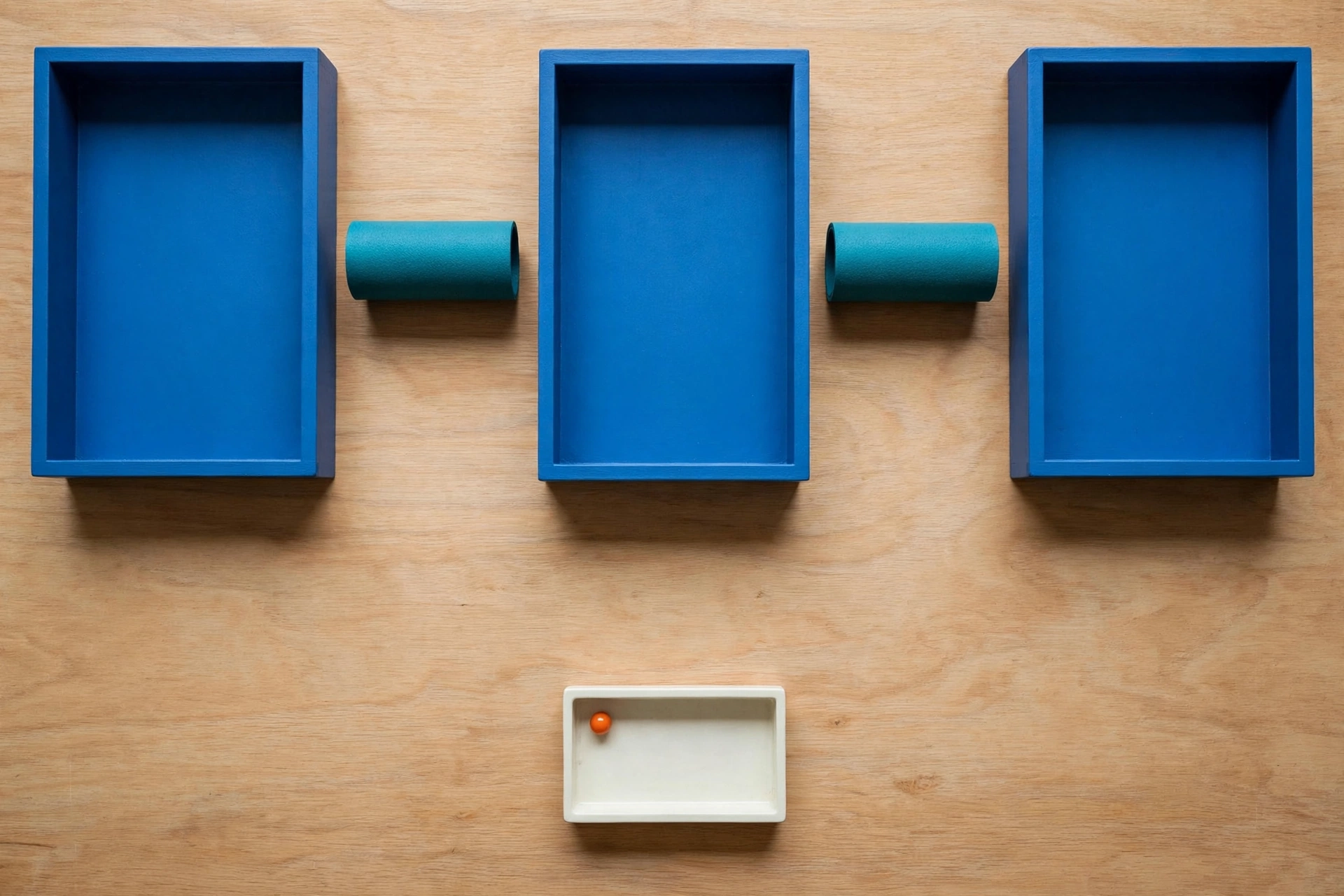 Three blue rectangular trays are arranged horizontally on a wooden surface, with two teal cylinders placed in the gaps between them.