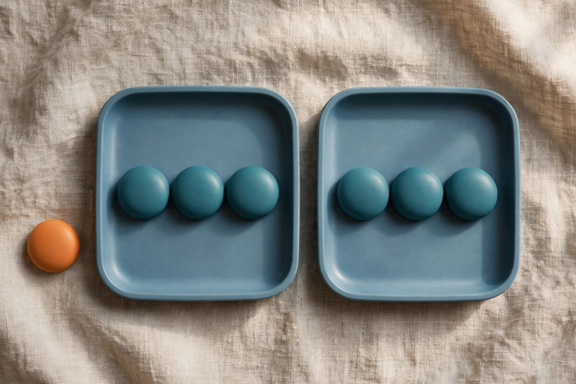 Two blue trays with teal tokens sit side-by-side on a textured surface, with an orange token placed beside one tray.