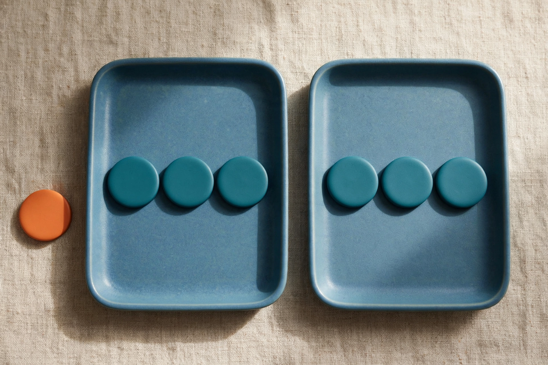 Two blue trays with teal tokens and one orange token outside sit on a textured surface.